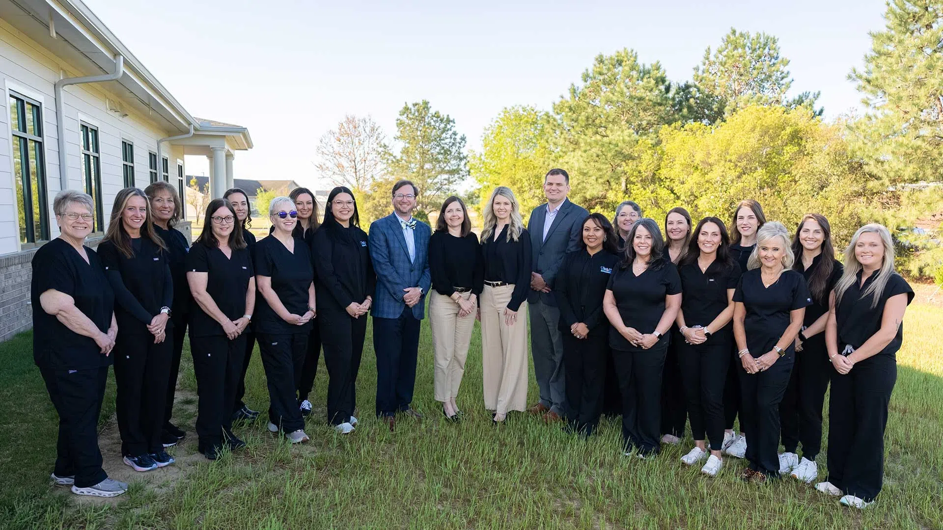 Group of medical professionals and staff posing outside a building on a sunny day with trees in background