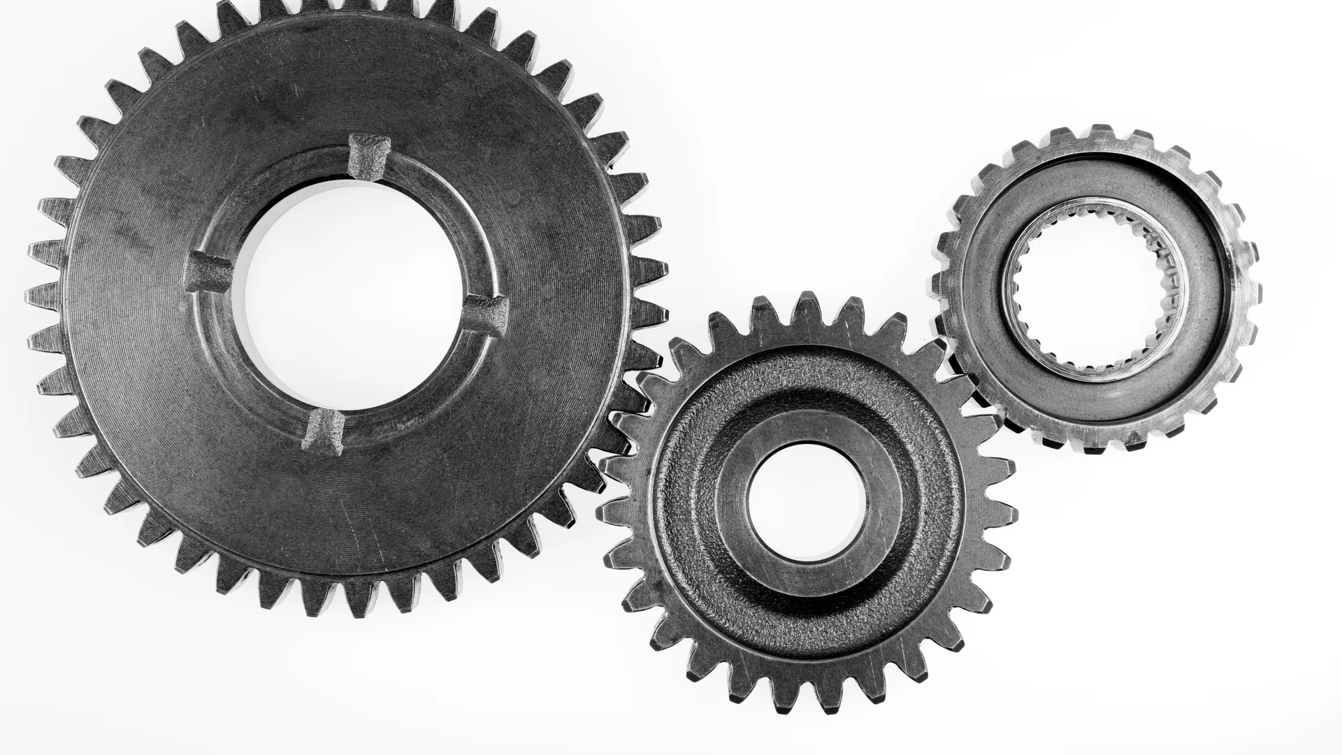 Three black metal gears of varying sizes arranged on a white background highlighting mechanical components.