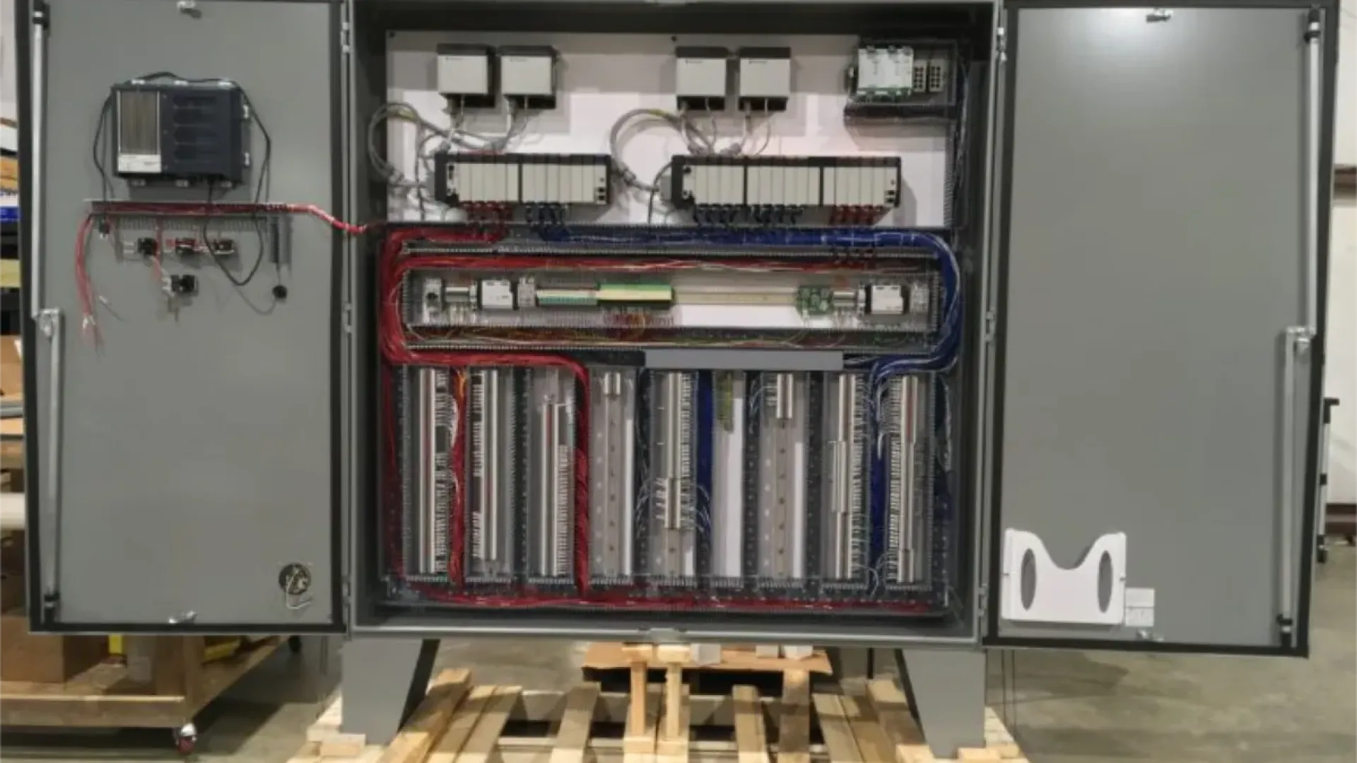 Open industrial control panel with organized wiring and electrical components mounted on pallet in warehouse.