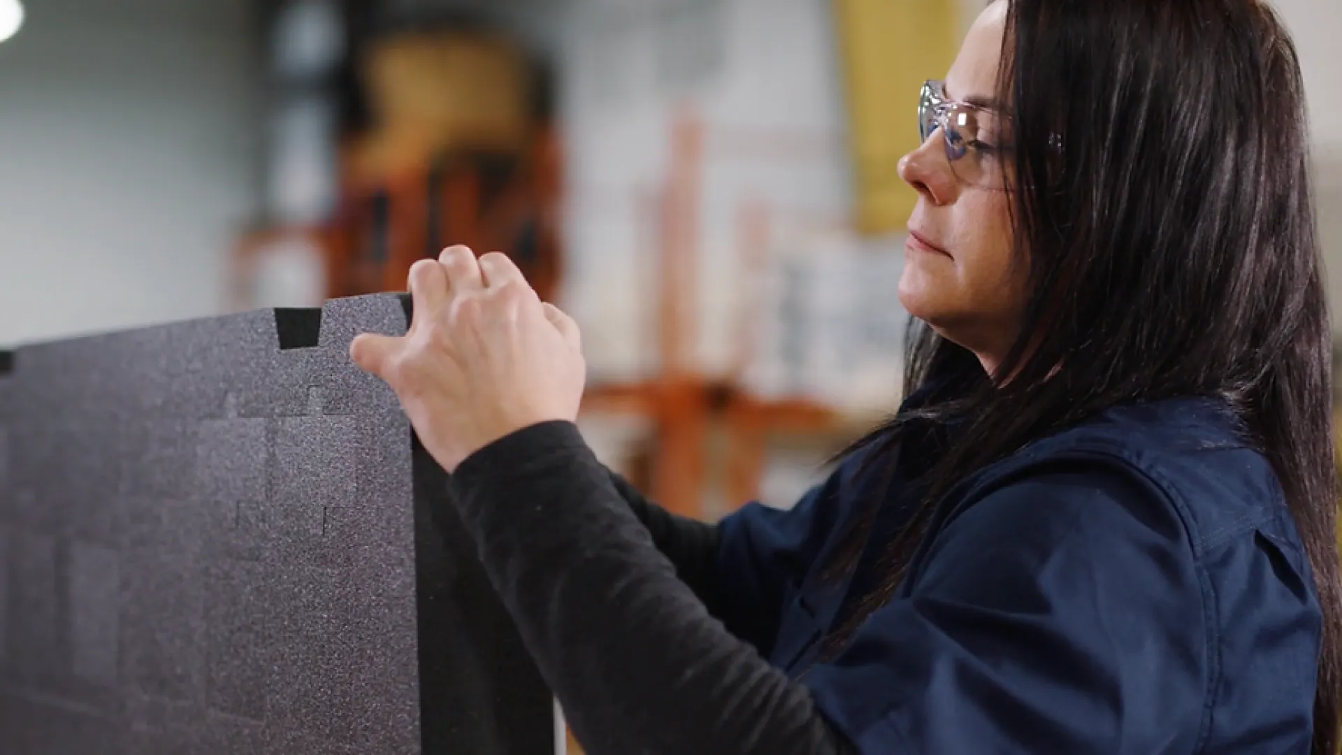 Woman wearing safety glasses assembling black foam panels in an industrial workspace
