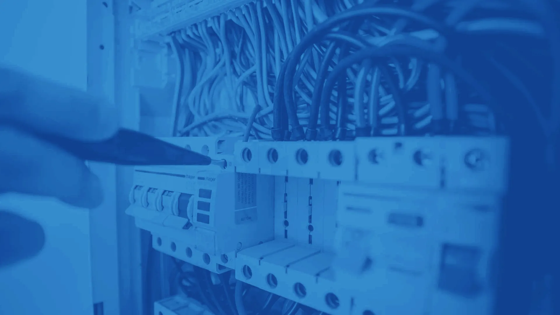 Hand inspecting electrical circuit breakers and wiring inside a control panel with a screwdriver.