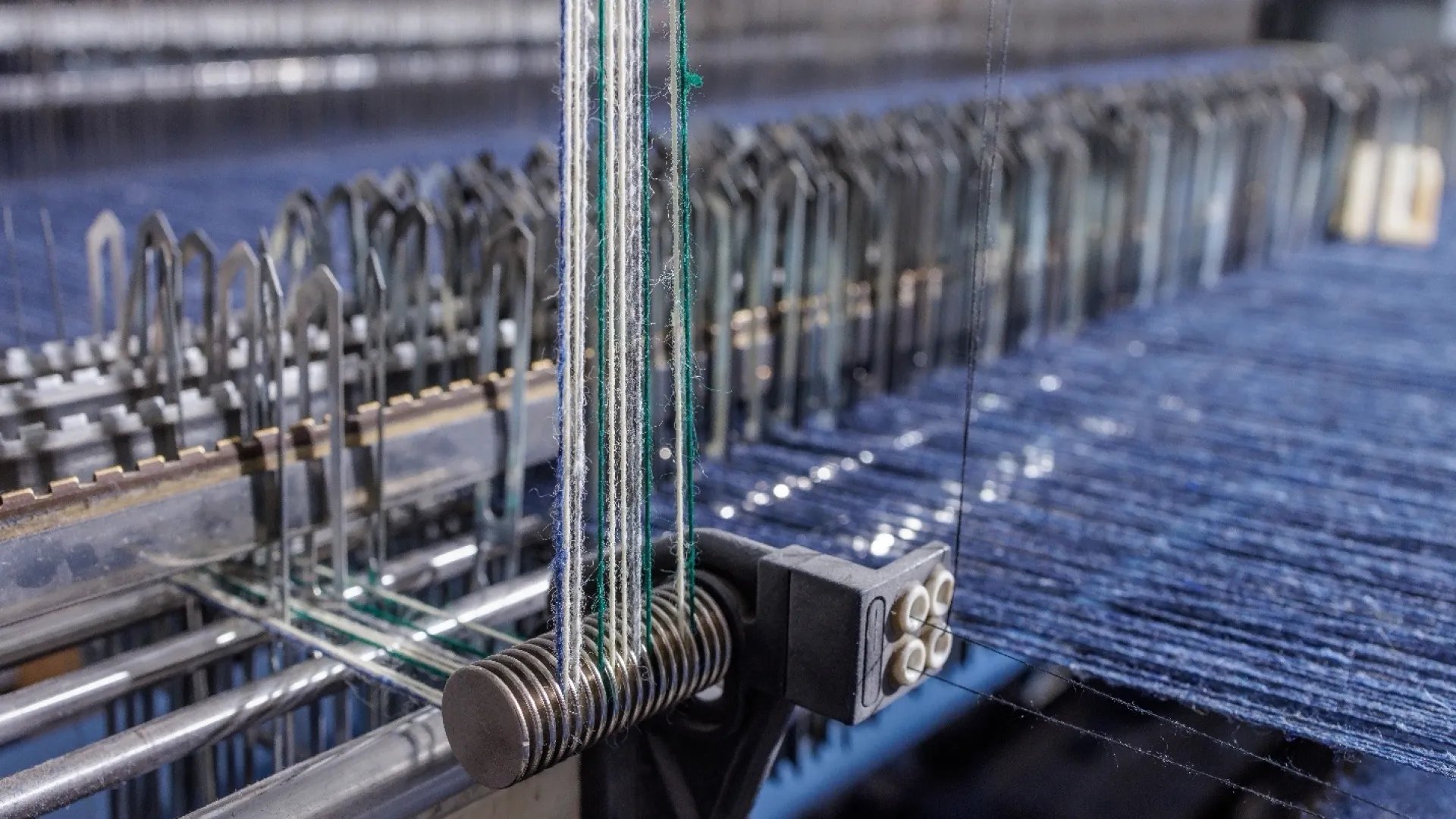 Close-up of industrial weaving machine with blue threads and metal components weaving fabric.