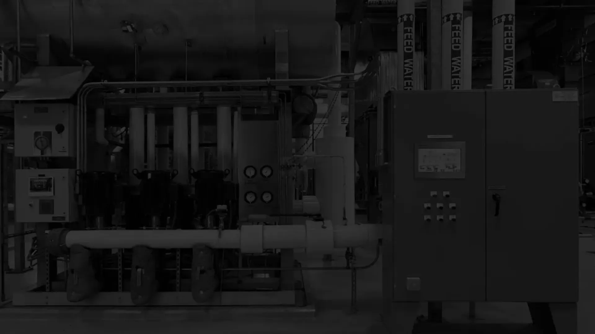 Industrial mechanical room with pipes, gauges, control panels, and large machinery in a factory setting.