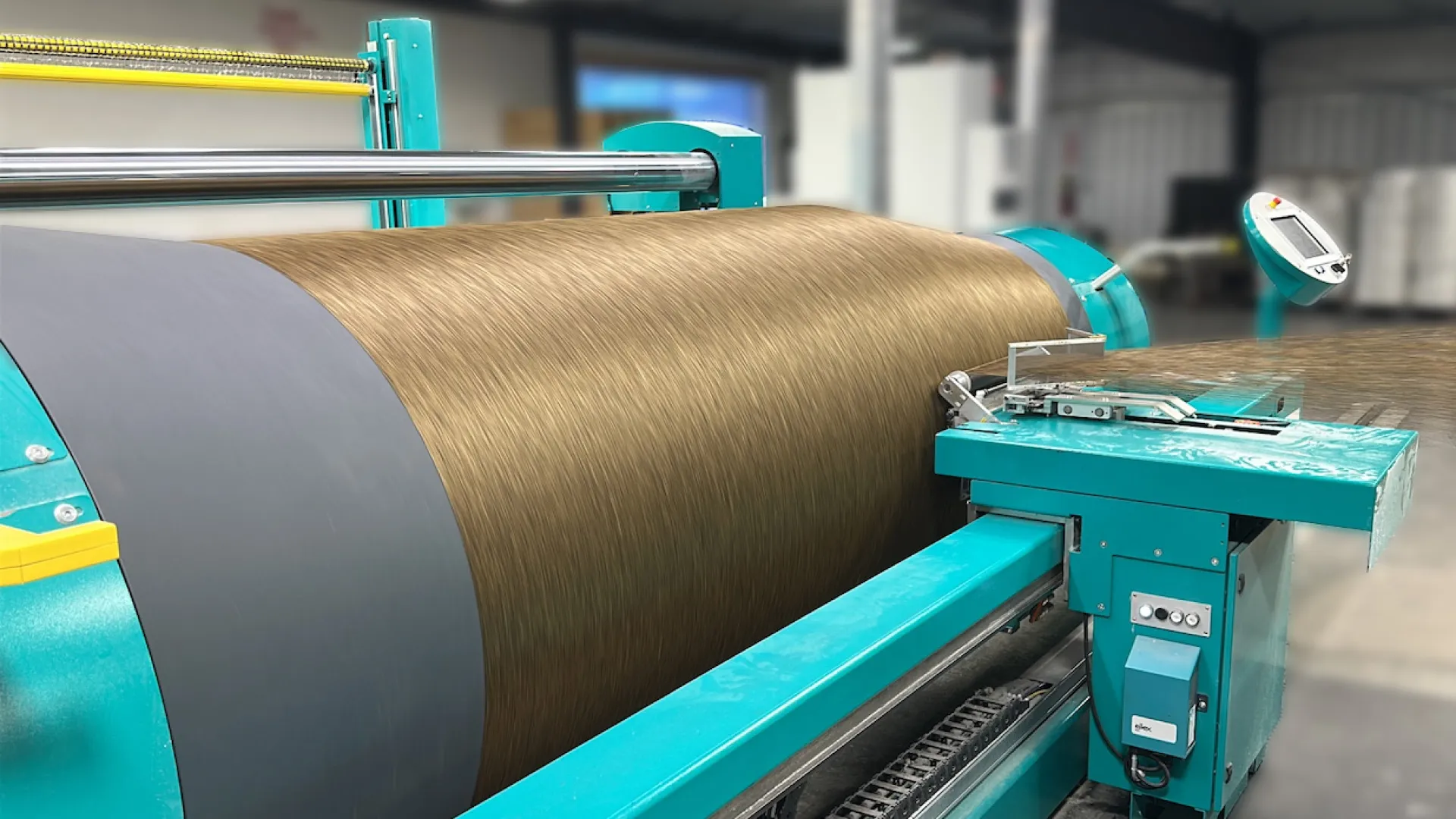 Industrial machine winding brown textile fiber in a factory setting with teal machinery components.