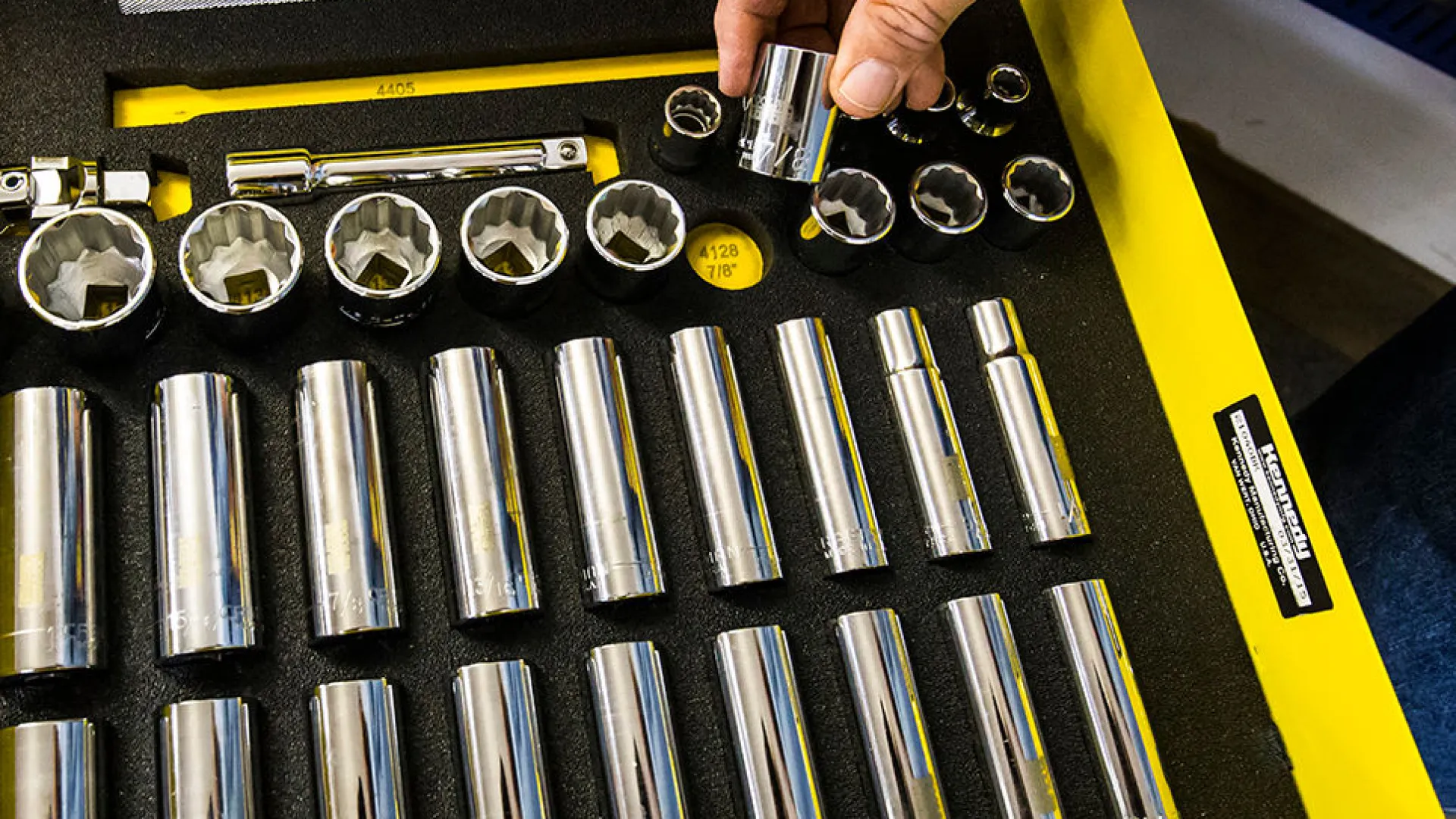 Hand picking a chrome socket from organized yellow tray with various socket wrench sizes and tools.