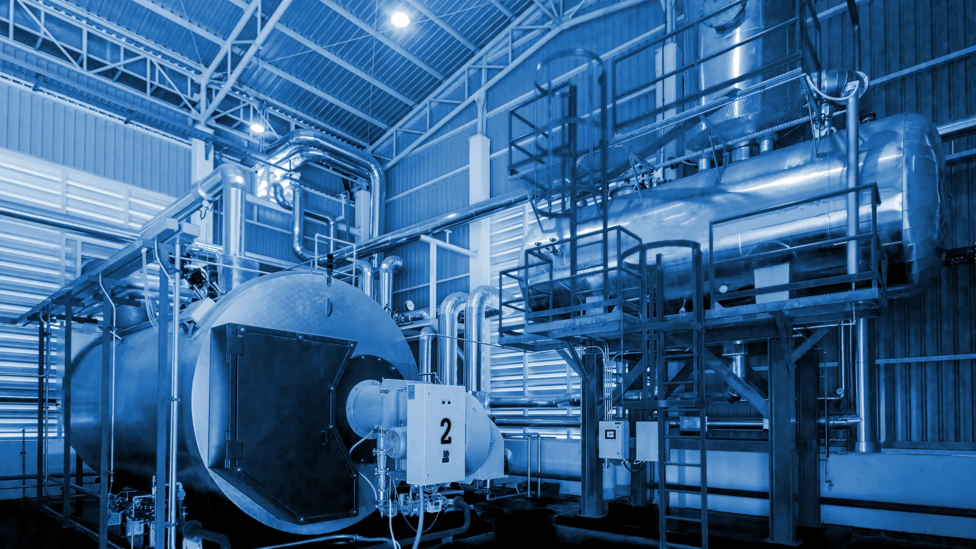 Industrial boiler system with large cylindrical tanks and metal pipes inside a factory building