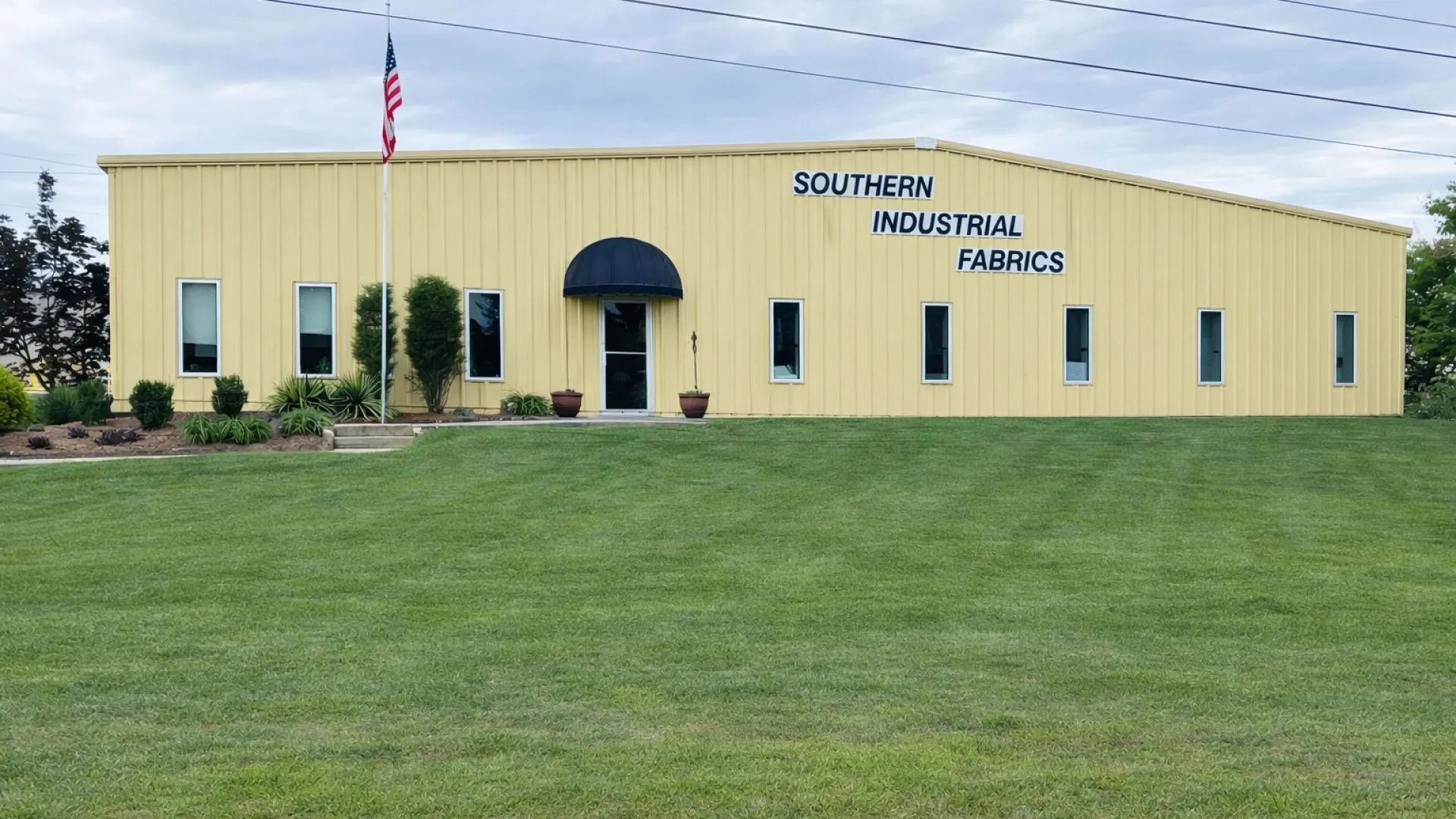 Yellow industrial building with Southern Industrial Fabrics sign on green lawn and American flag.