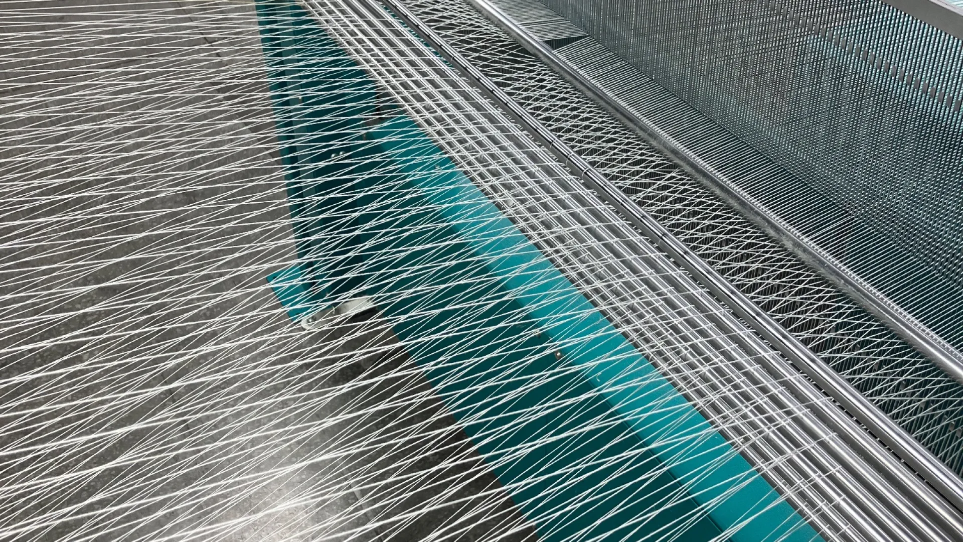 Industrial textile machine with multiple white threads stretched and aligned in a large factory setting.