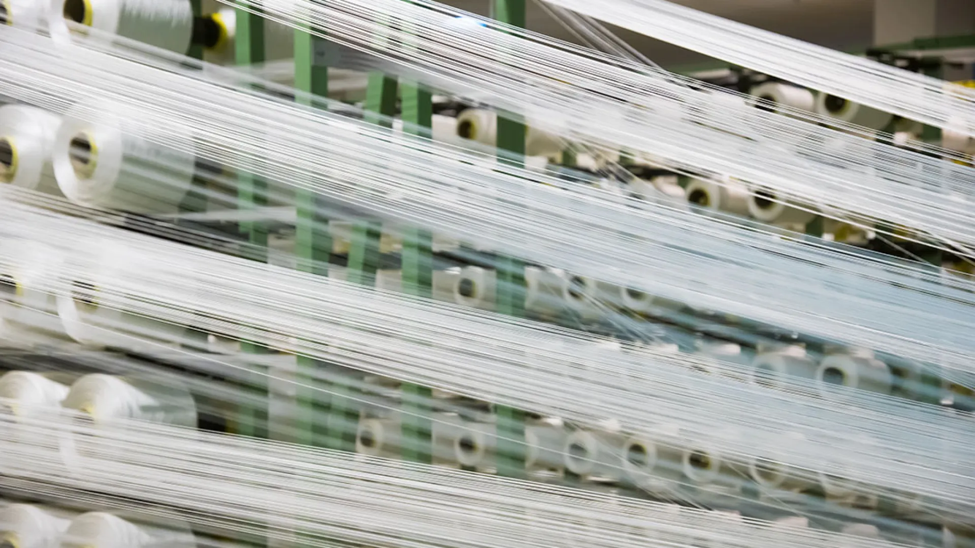 Industrial textile machine with multiple spools of white thread stretched and aligned in a factory setting.