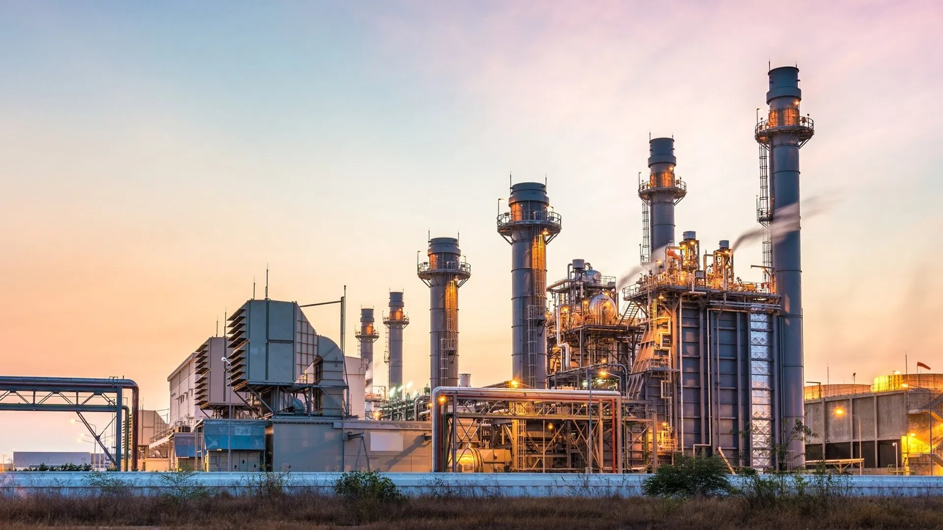 Industrial power plant with multiple smokestacks emitting steam during a colorful sunset sky.