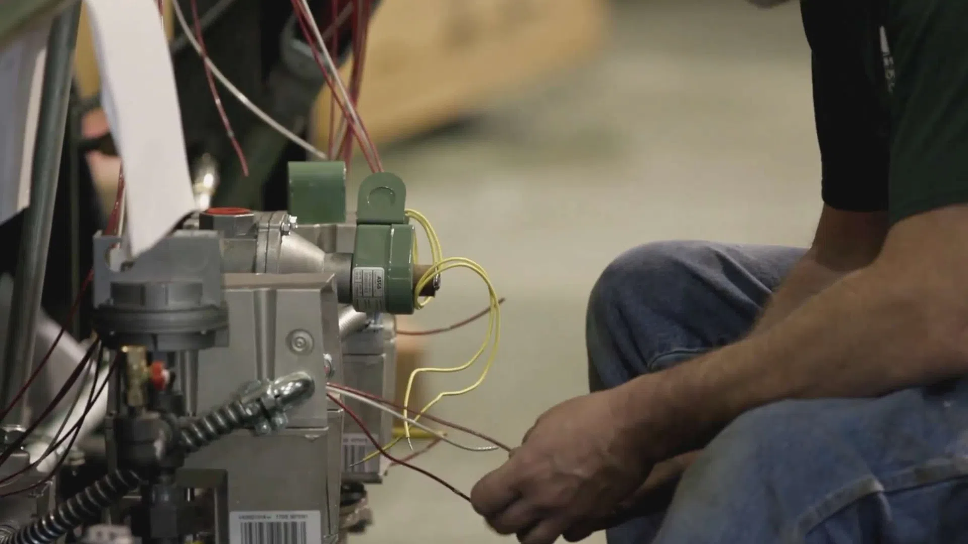 Technician working on complex gas valve and wiring in industrial equipment, focusing on connections and components.