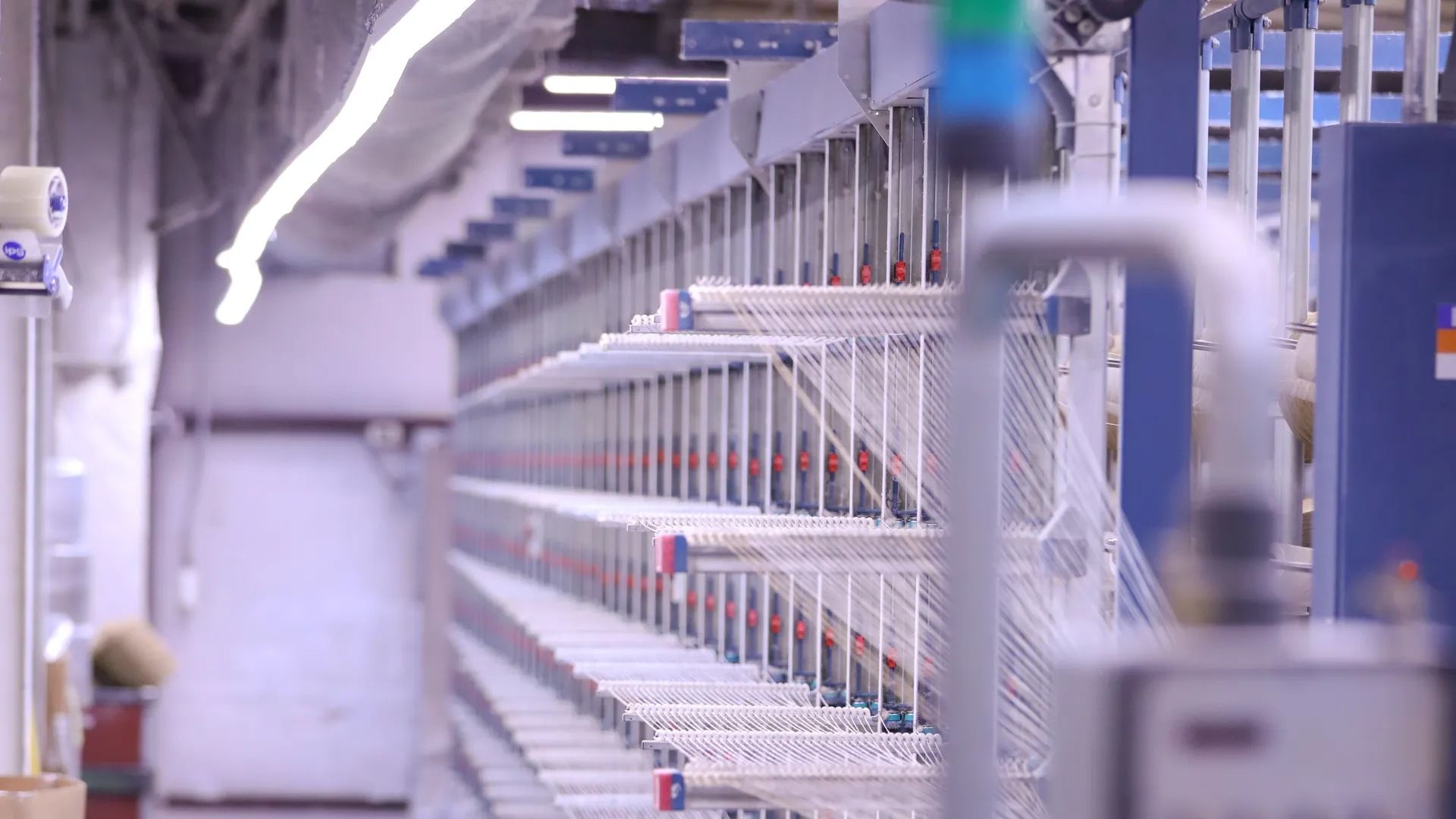Textile factory interior with rows of machines spinning white yarn on spindles under industrial lighting.