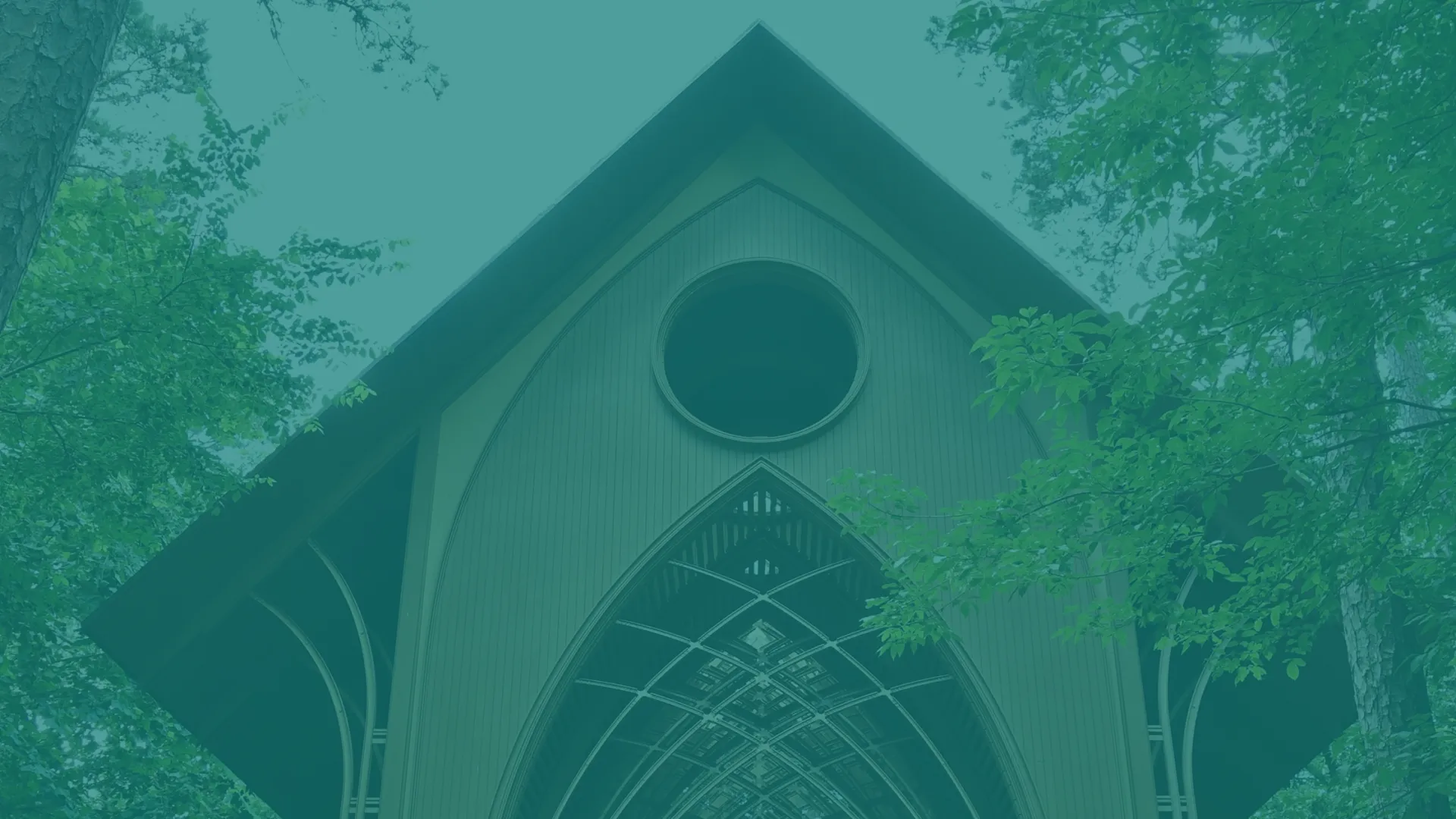 A tall triangular roof structure surrounded by lush green trees, showcasing modern architecture.