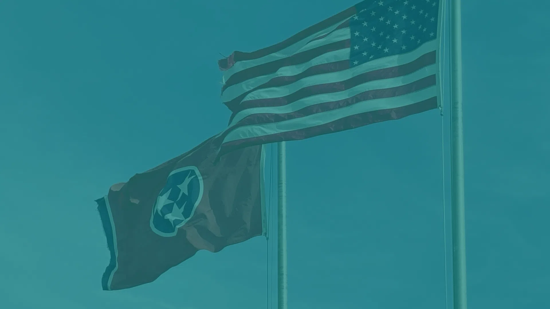 American and Tennessee state flags waving on flagpoles against a clear blue sky.