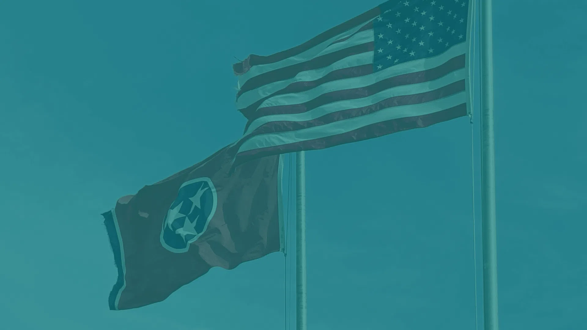 American and Tennessee state flags waving on flagpoles against a clear blue sky.