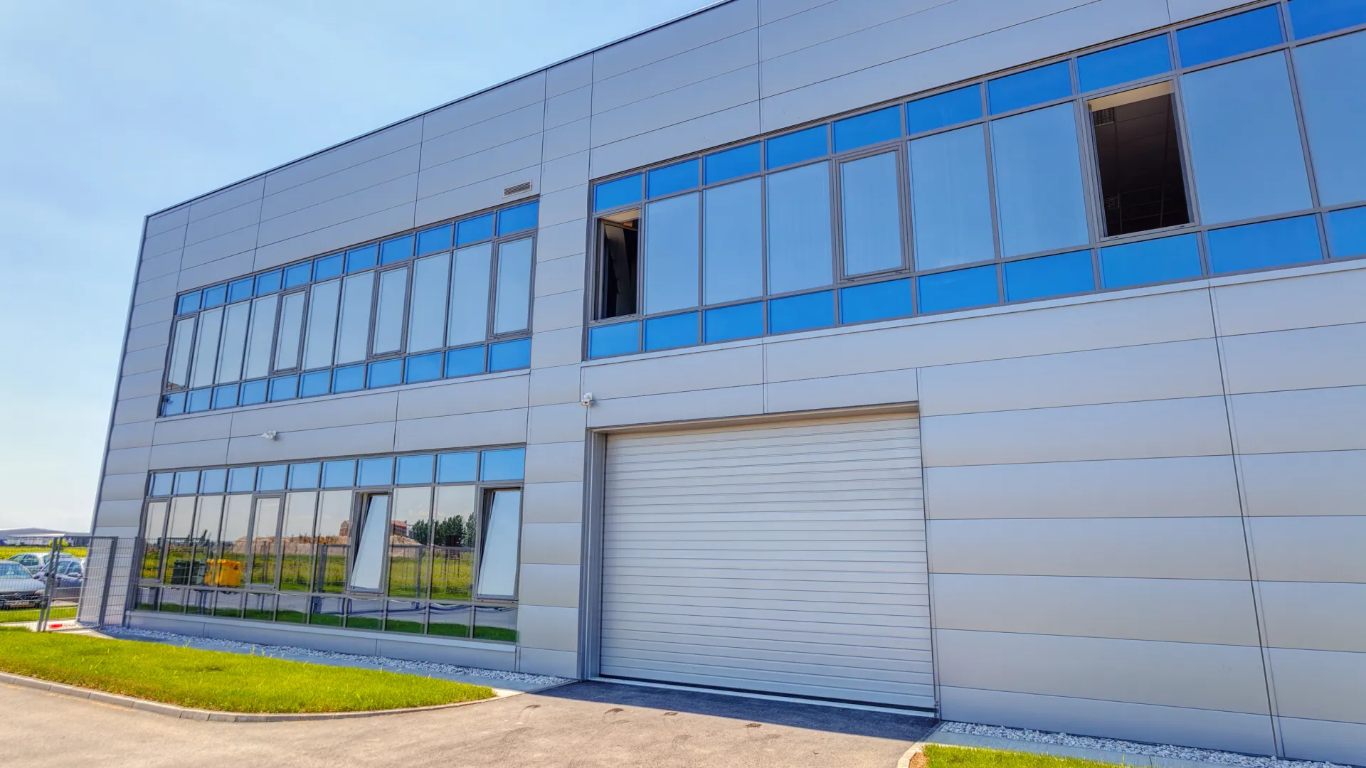 Modern commercial building with large reflective windows, metal panels, and a closed white garage door under clear sky