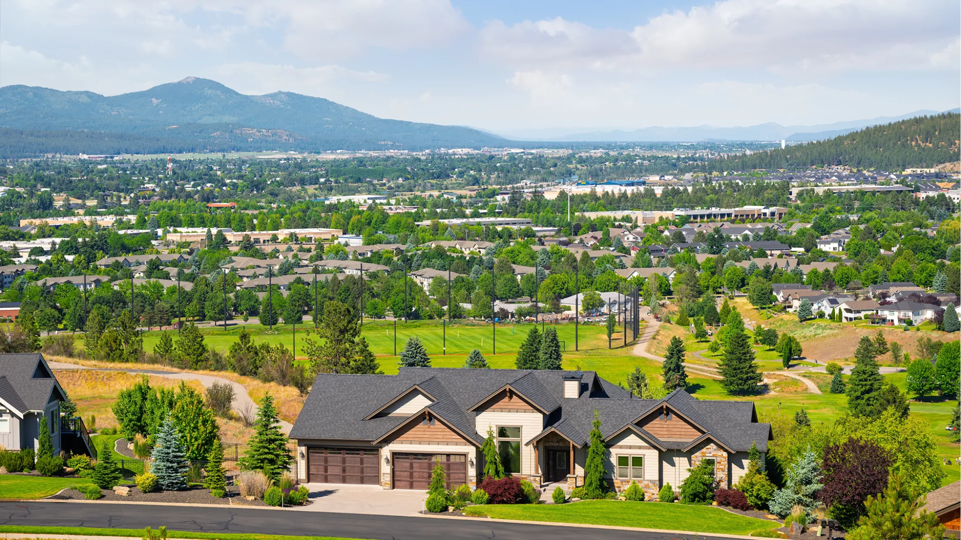 Spacious suburban home with landscaped yard overlooking a green golf course and distant mountains under a blue sky.
