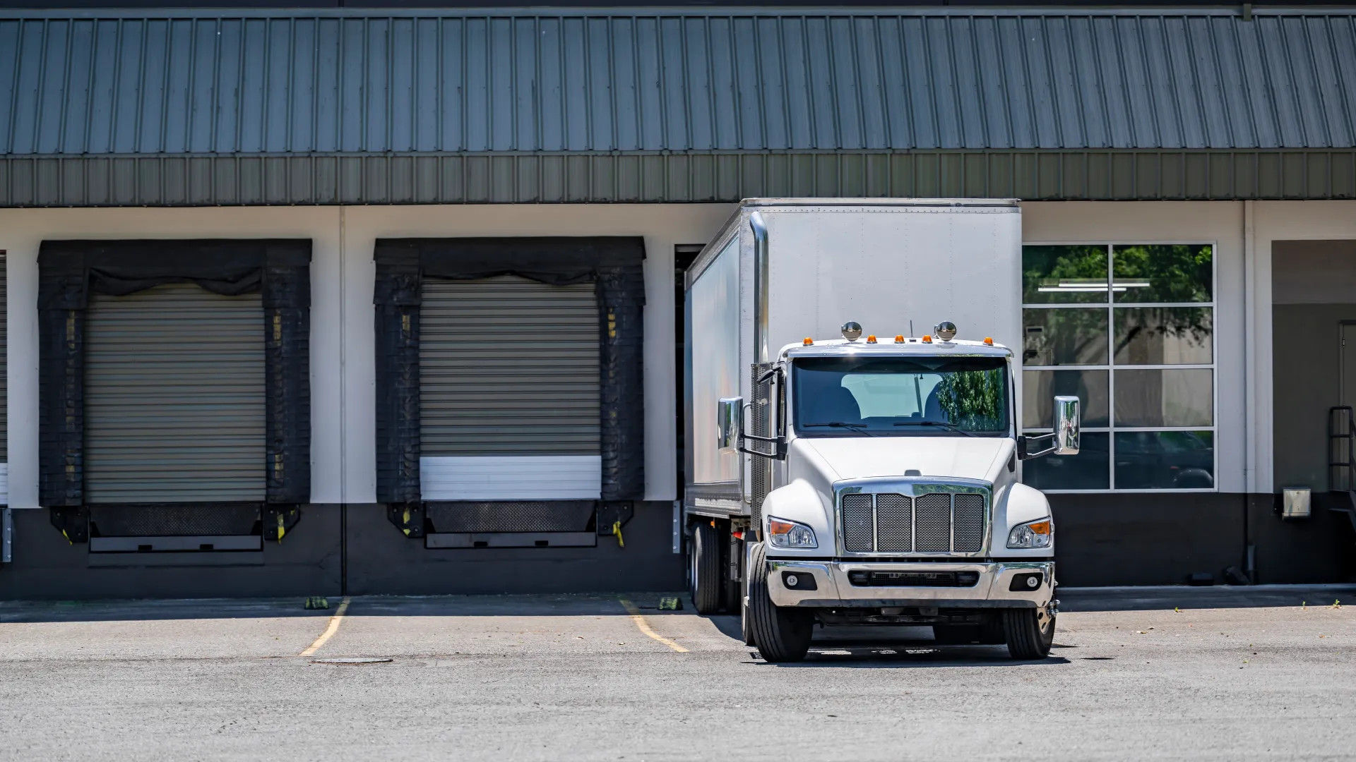 White semi-truck parked in front of closed loading dock doors at a warehouse on a sunny day