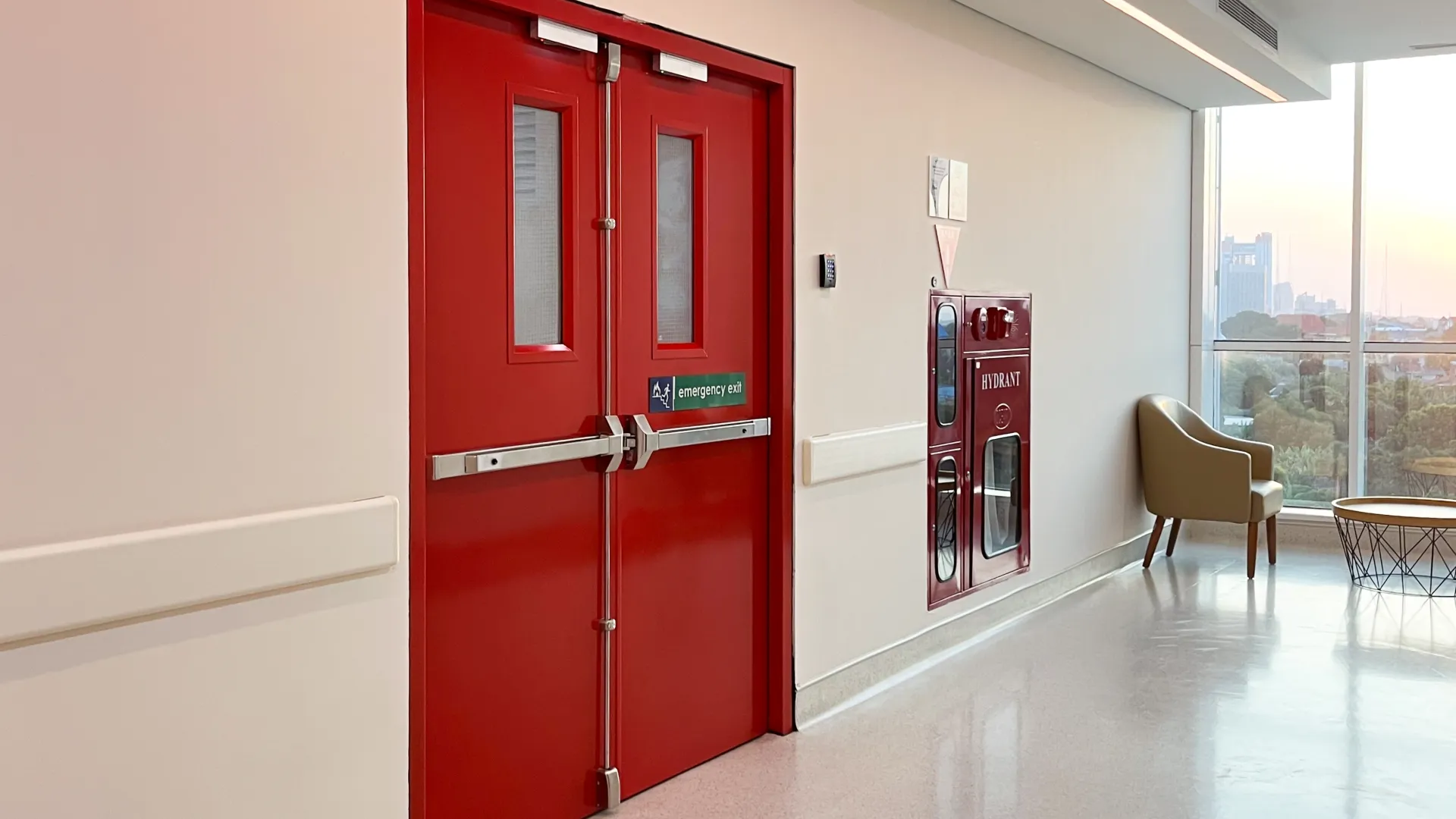 Bright red emergency exit door and fire hydrant cabinet in a clean, modern hallway with natural light.