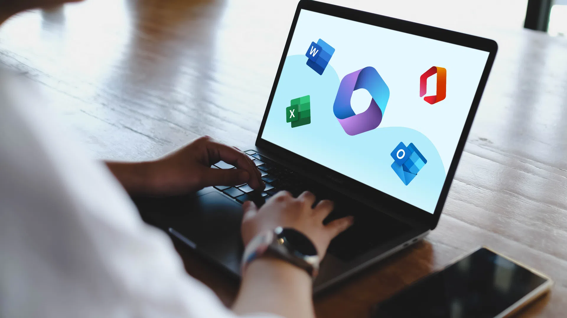 Person using laptop showing Microsoft Office app icons including Word, Excel, Outlook on screen.