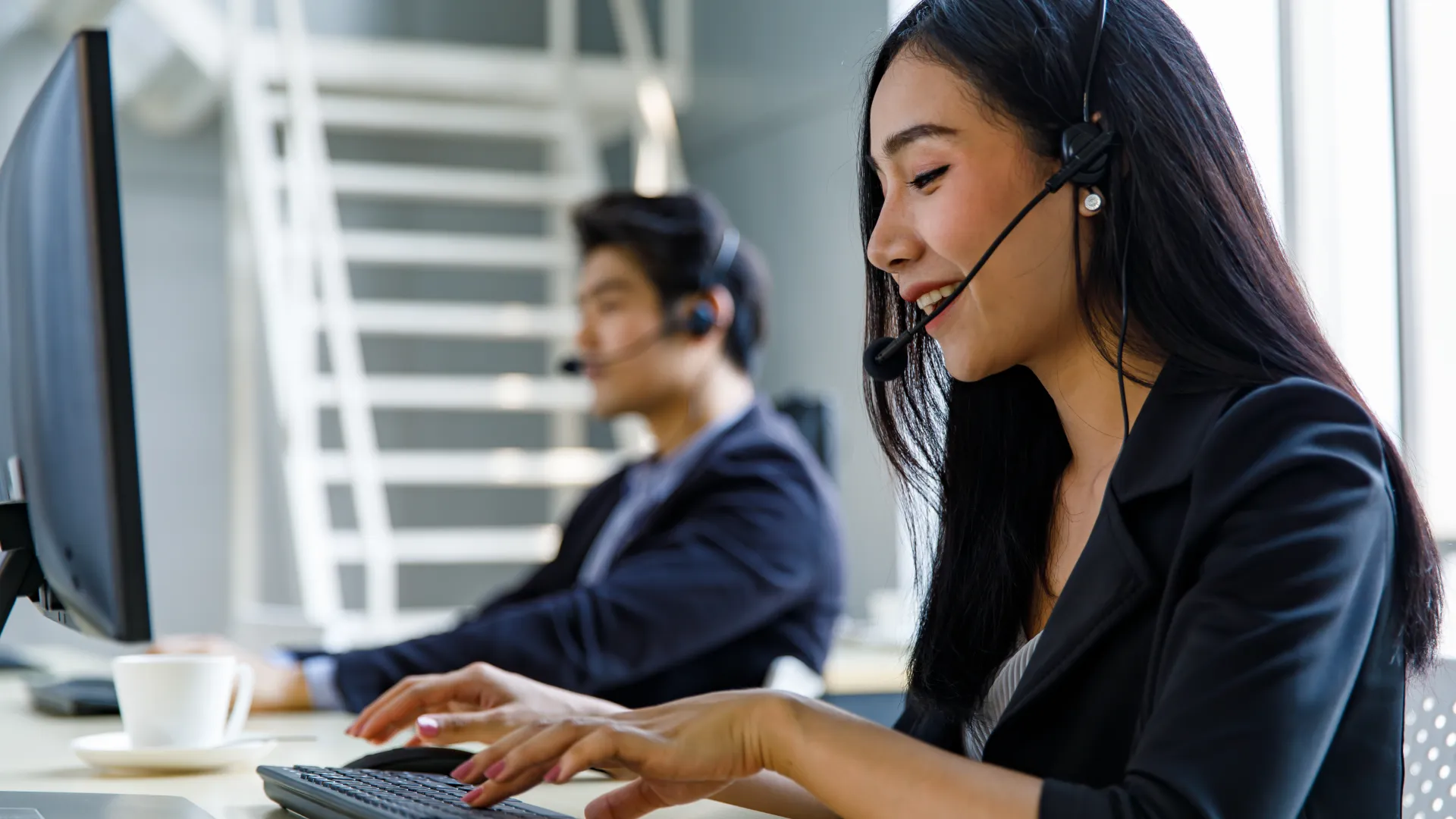 Female and male call center agents wearing headsets working at computers in a bright office environment
