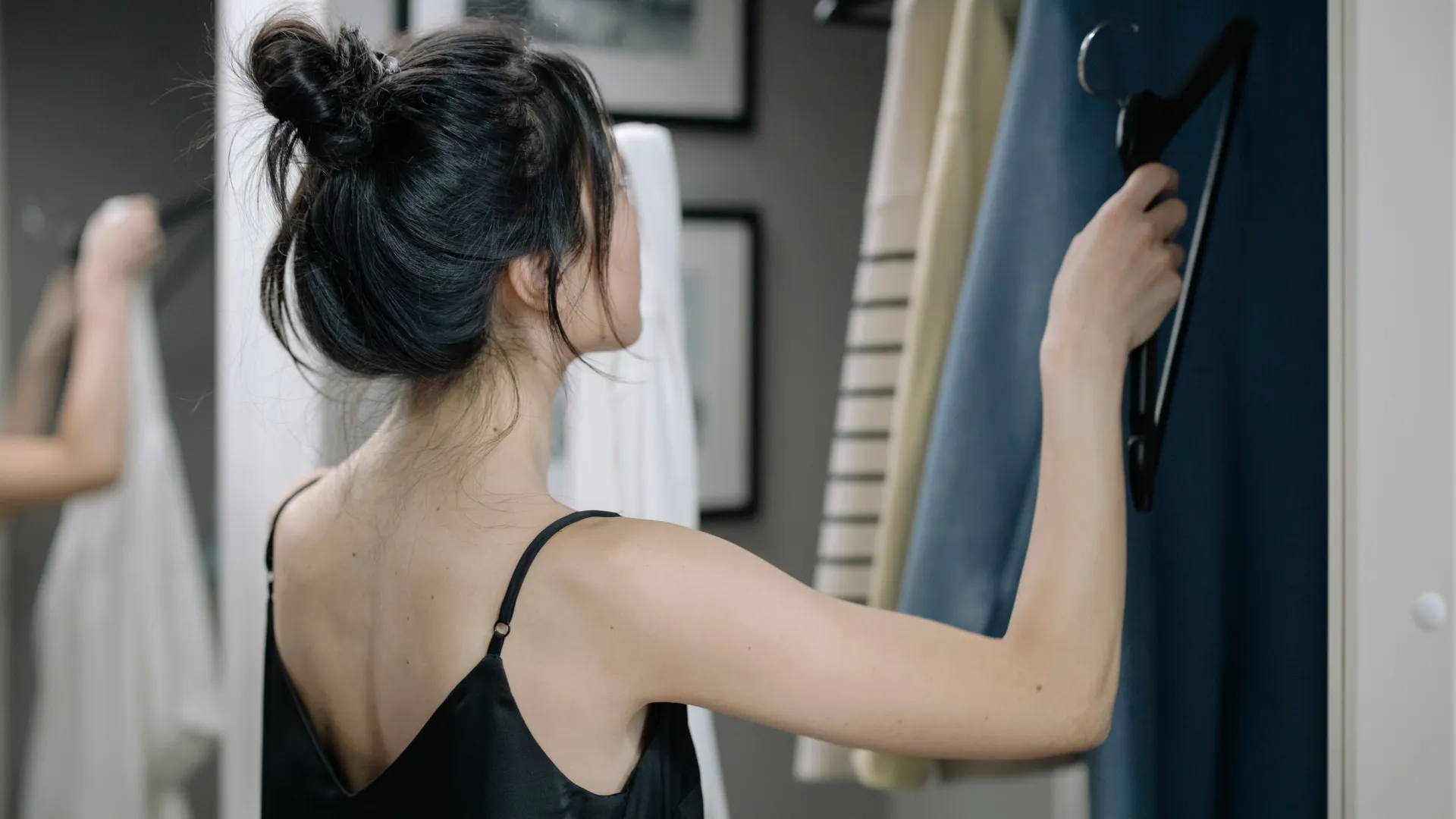 a woman in a black tank top looking at sweater hanging in a closet