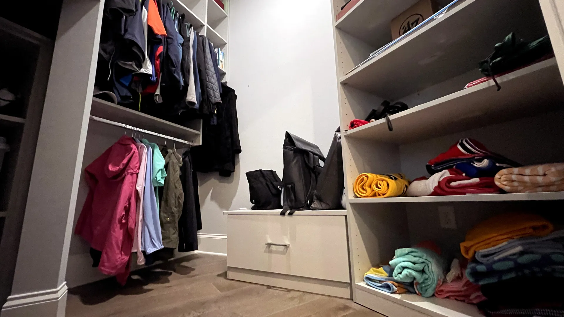 a small, weirdly shaped closet with clothes and shoes