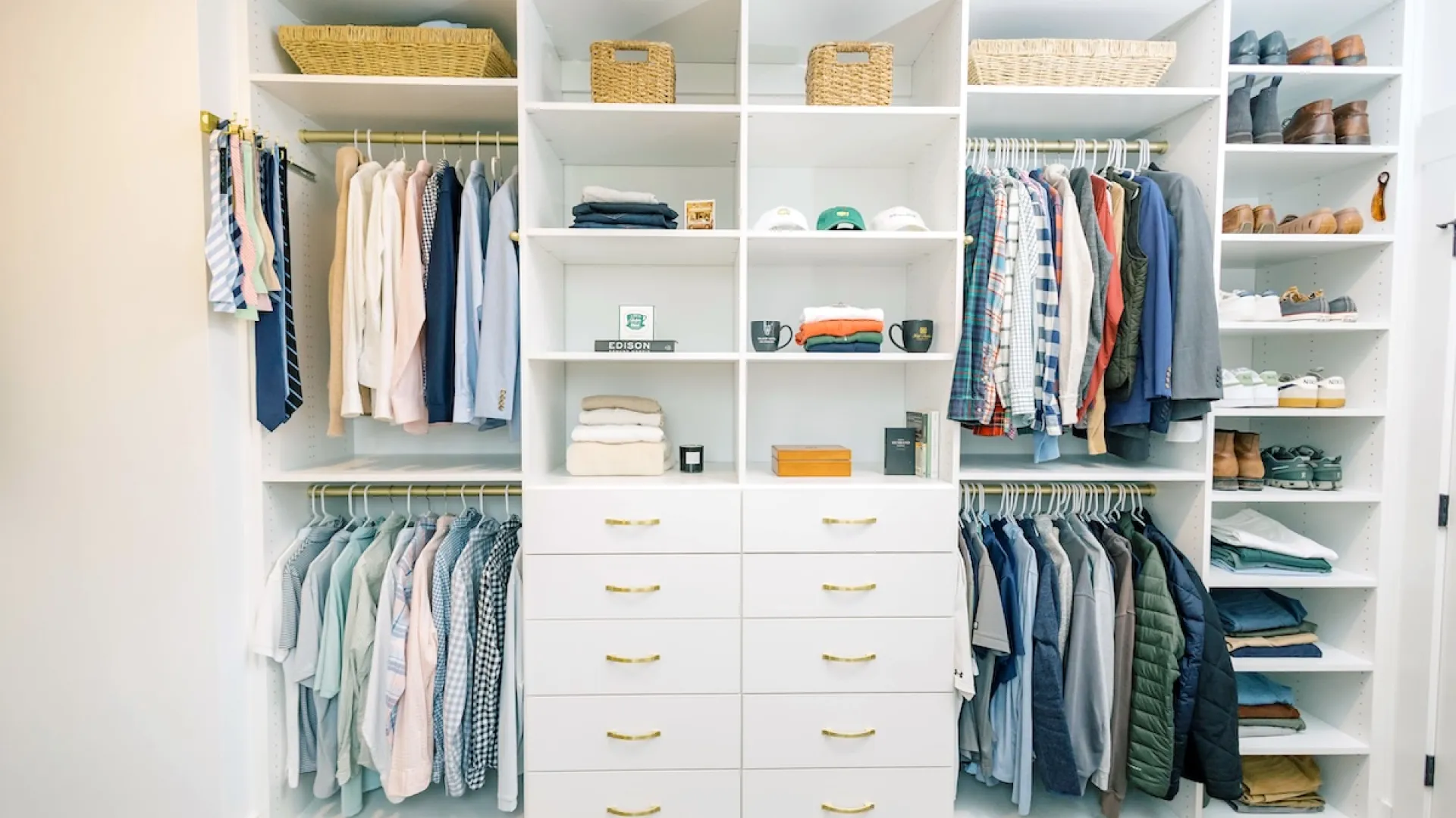 Organized white walk-in closet with hanging clothes, shelves, wicker baskets, folded items, and shoes on racks.
