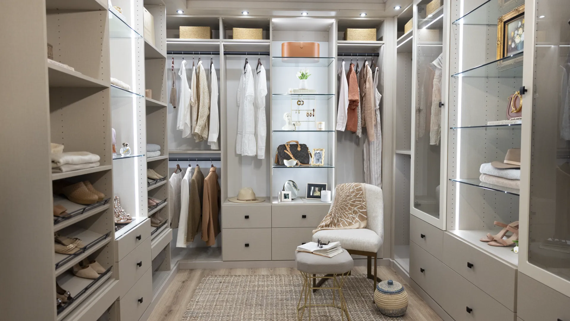 a custom built master closet with clothes and a chair