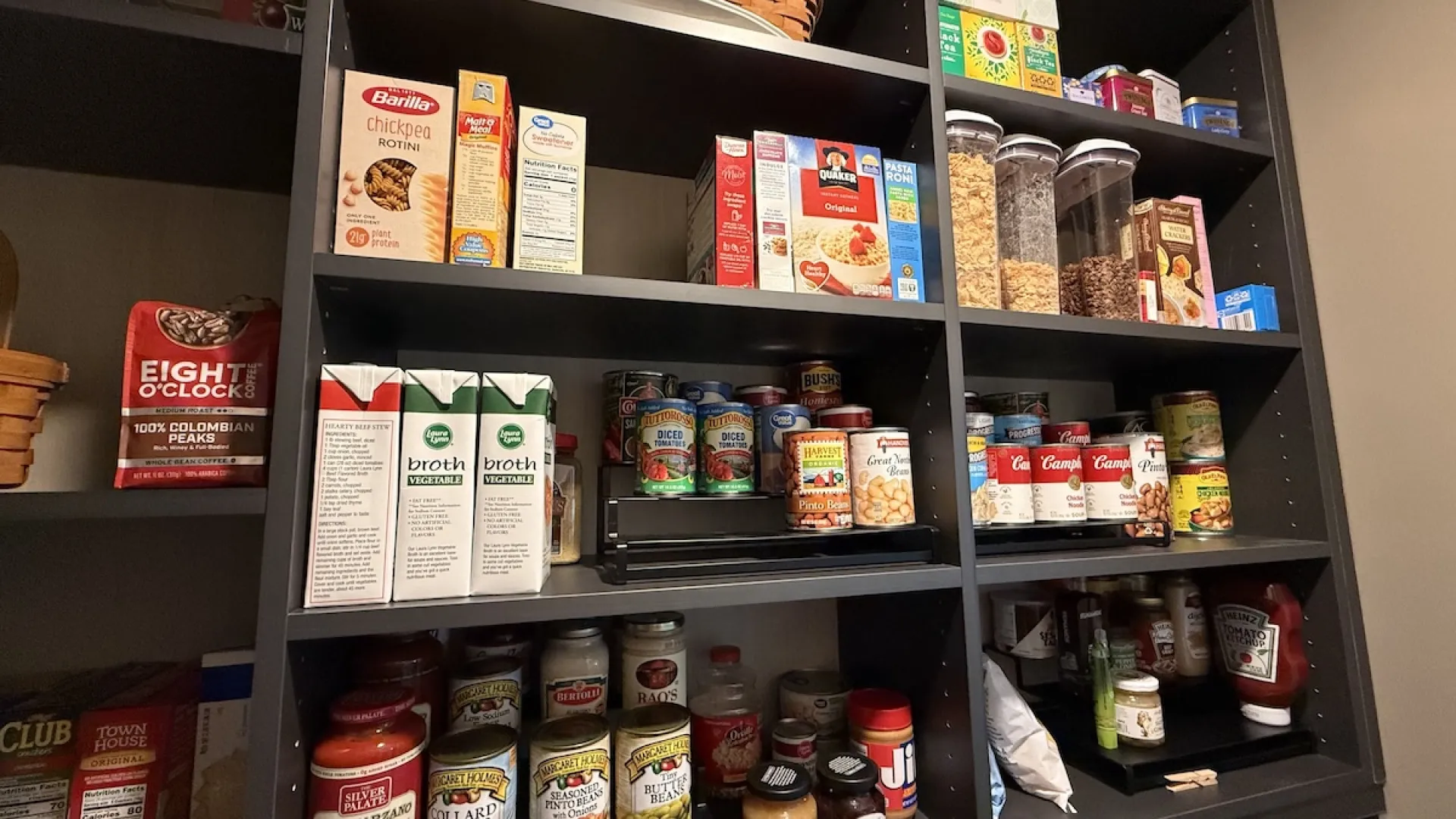 Organized kitchen pantry shelves with canned goods, cereals in jars, pasta, broth boxes, and condiments.