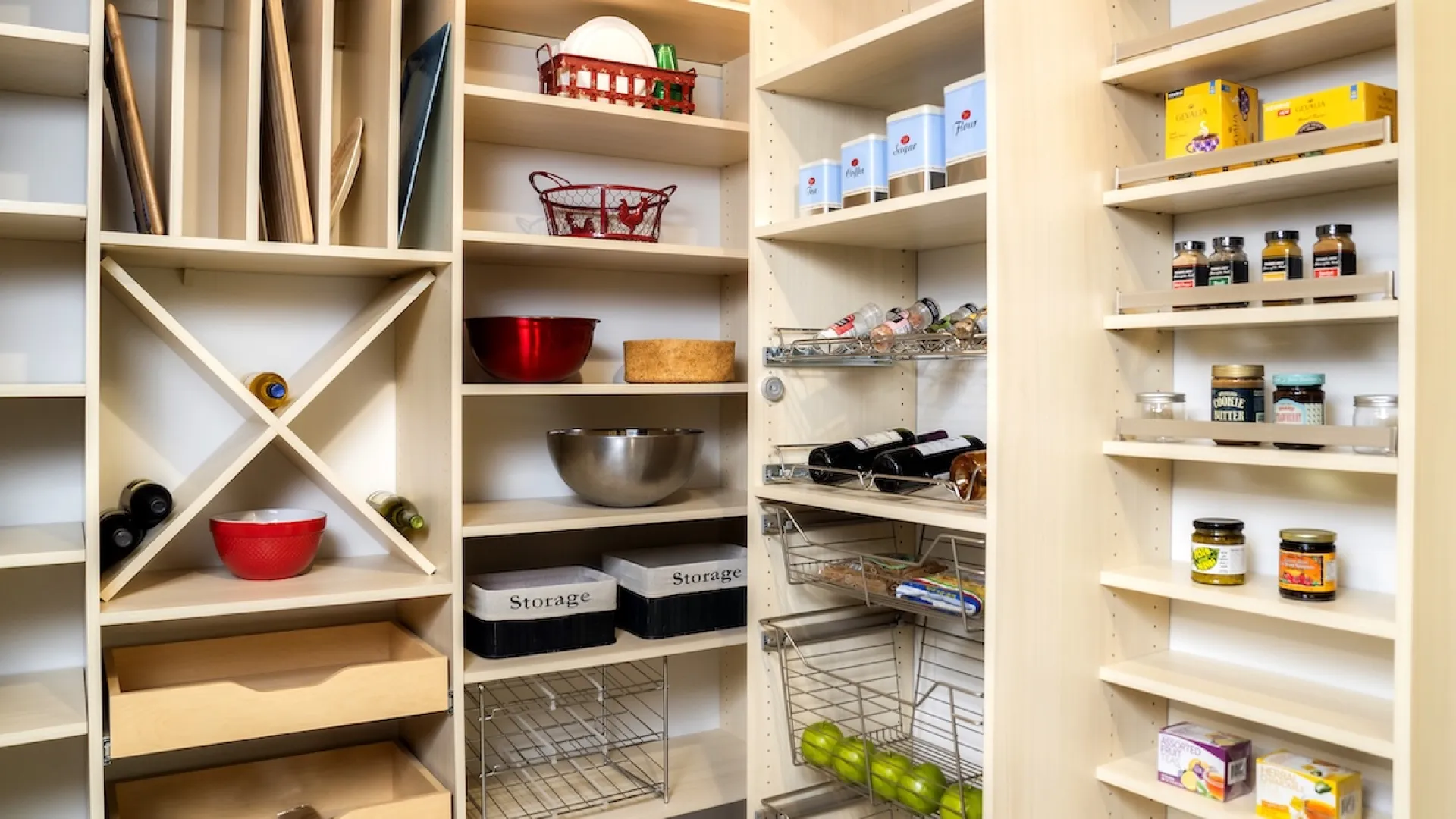 Organized pantry shelves with wine racks, storage bins, bowls, canned goods, and fresh produce like apples.