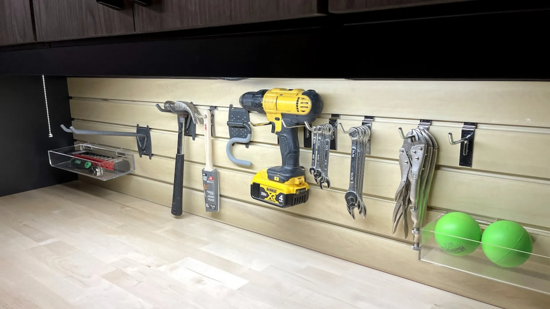Organized workshop wall with tools including drill, hammer, wrenches, pliers, and green balls on a wooden countertop.