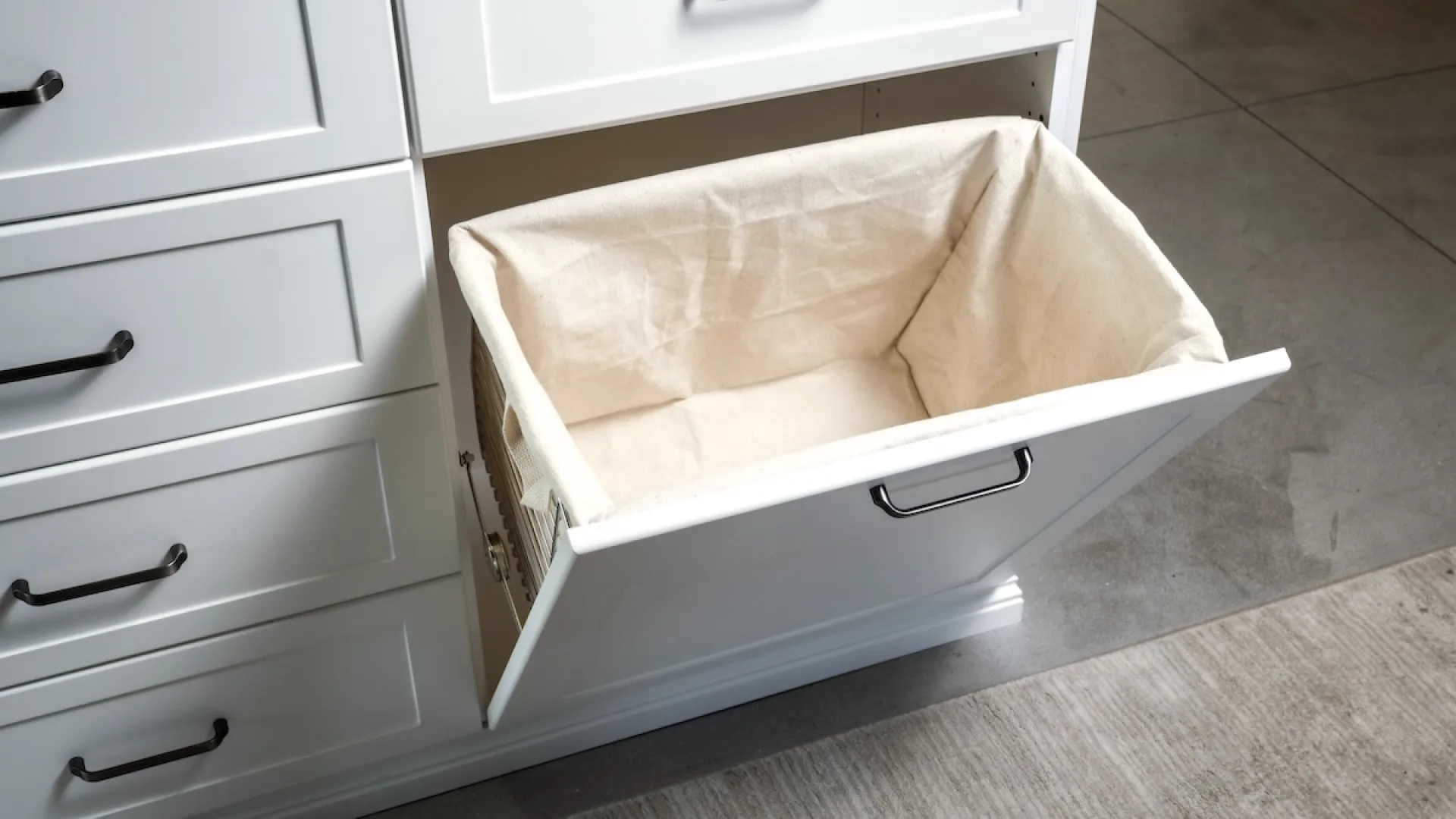 Open white pull-out laundry hamper with beige fabric liner integrated in modern cabinetry.