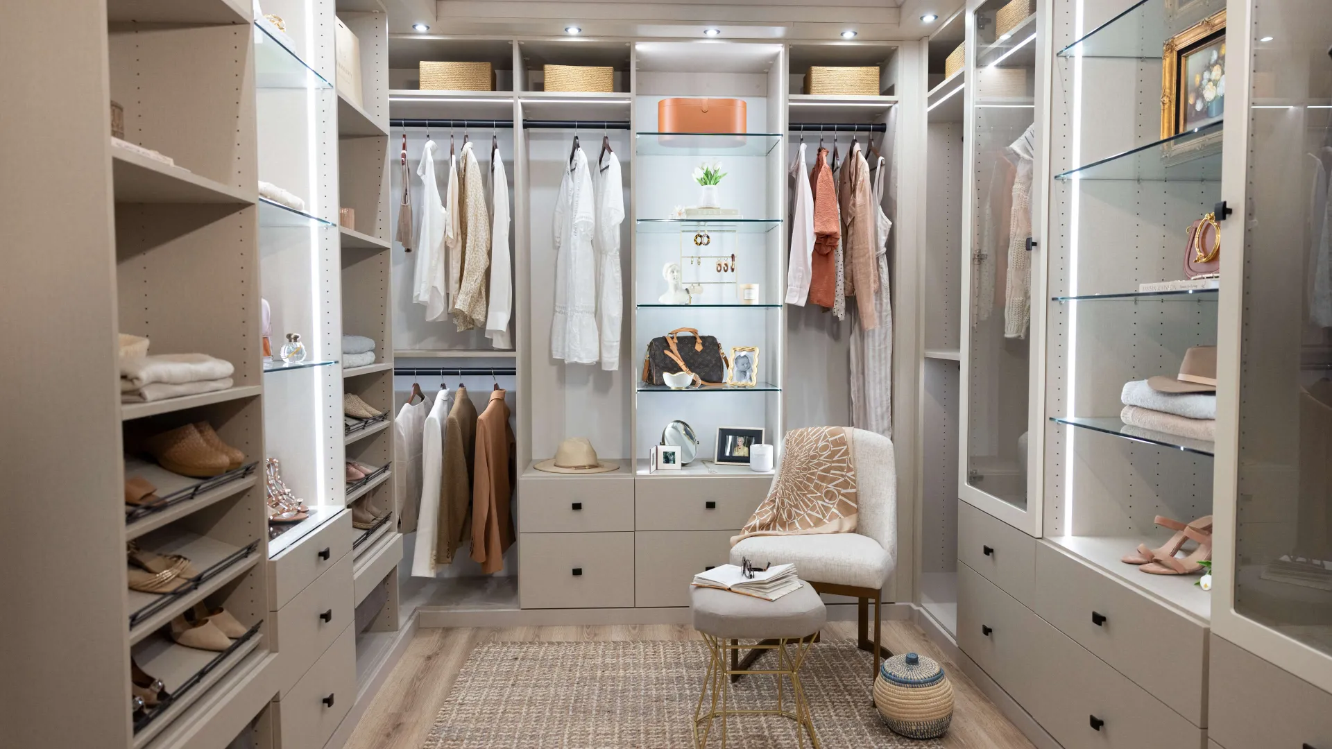 Elegant walk-in closet featuring organized shelves, stylish clothes, and a cozy chair for a luxe touch.