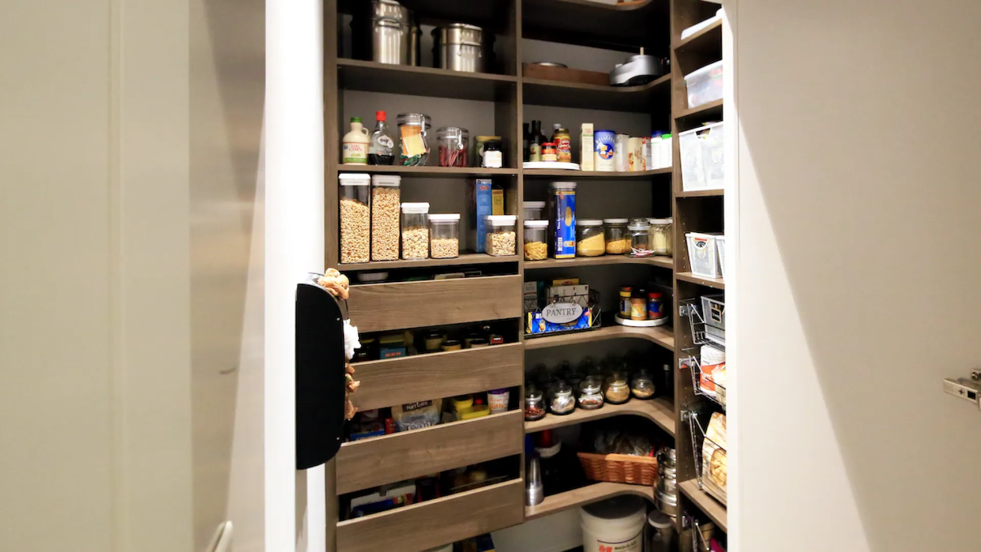 Organized pantry with shelves holding jars, cans, boxes, and kitchen essentials in a well-lit small room.