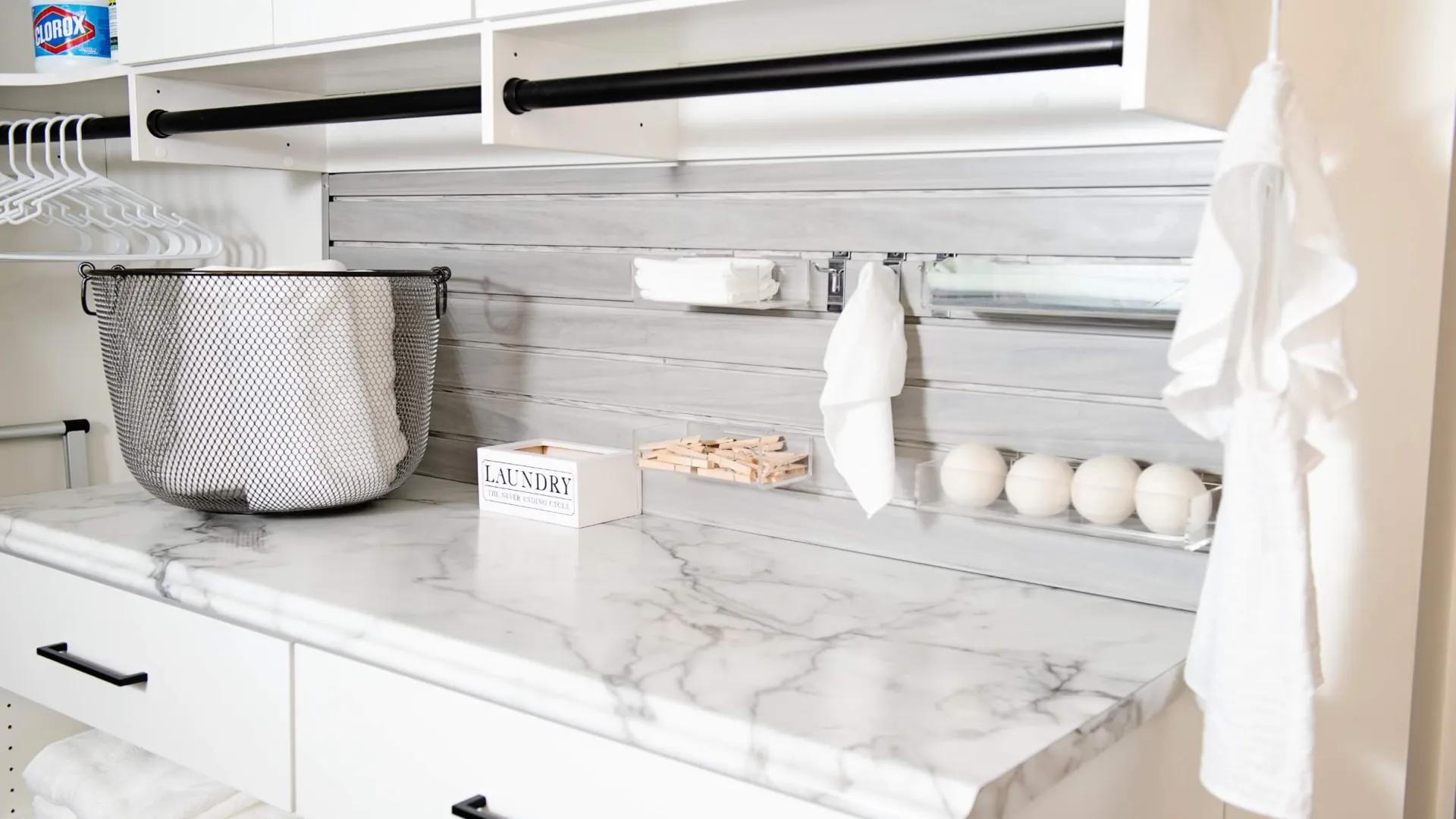Modern laundry room with marble countertop, white cabinets, hanging rod for clothing, mesh laundry basket and laundry supplies