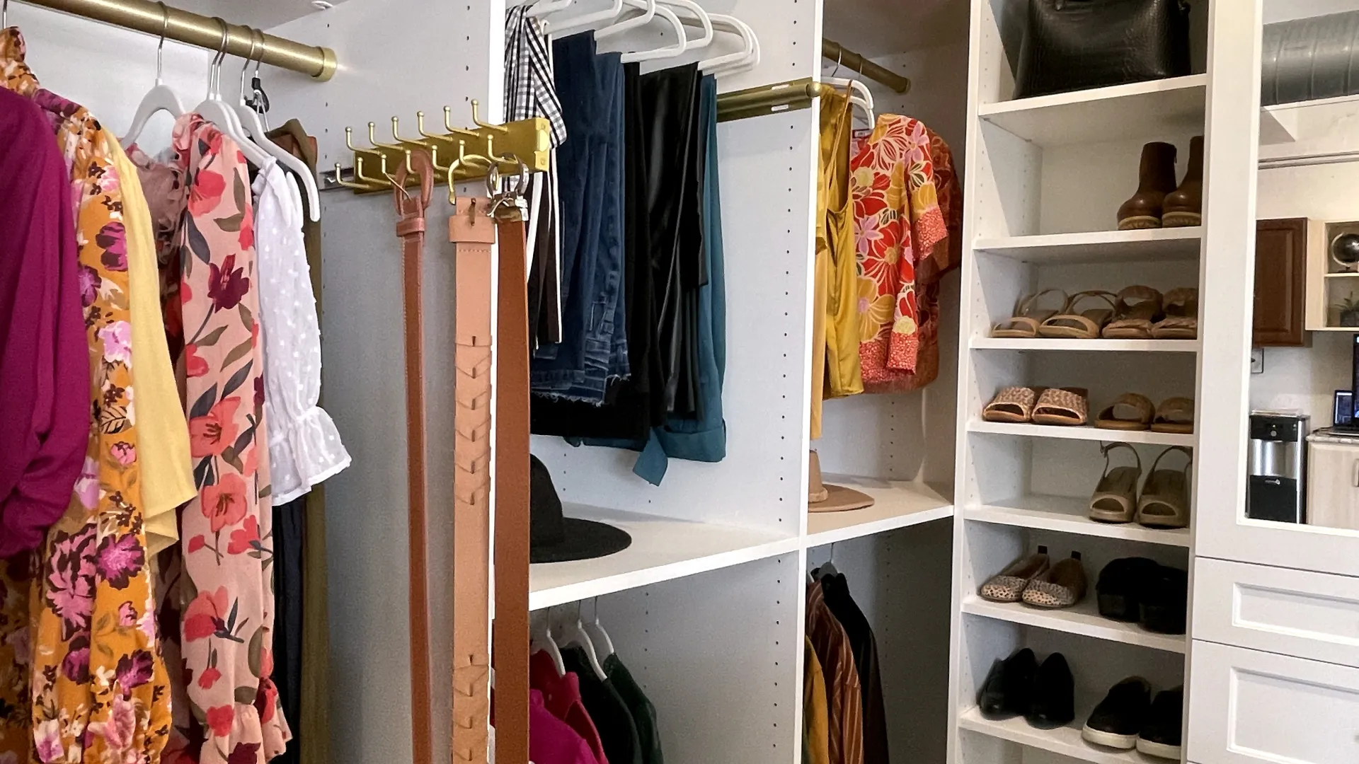 Organized walk-in closet with hanging floral clothes, belts, jeans, and neatly arranged shoes on shelves.