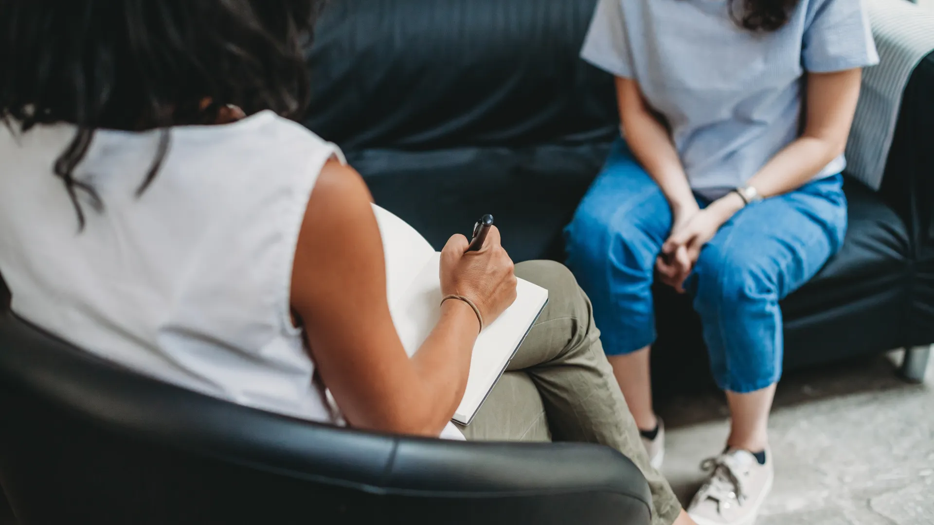 Therapist taking notes during a counseling session with a woman sitting on a sofa in a modern office.