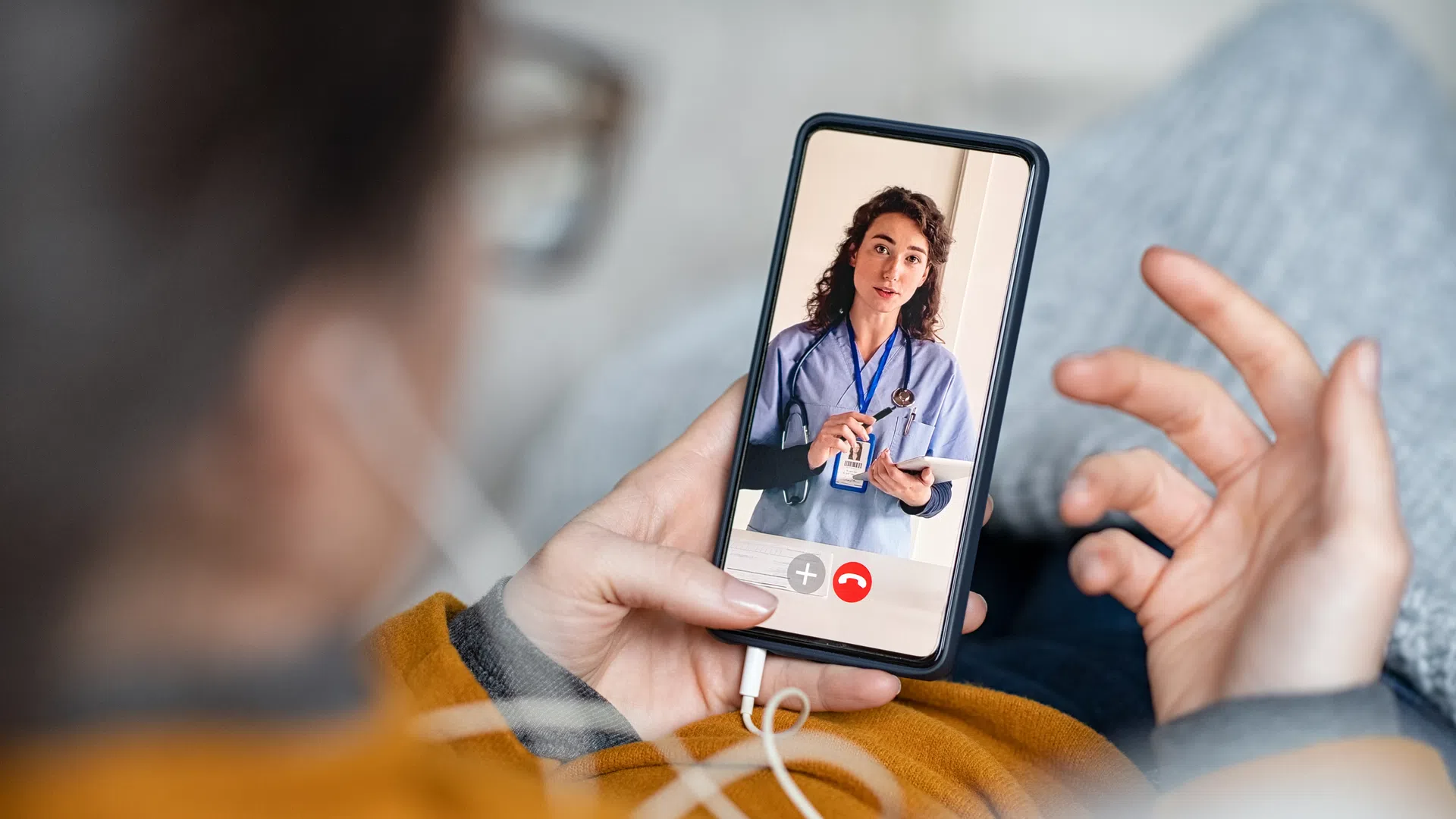 Person holding smartphone having a video call with a female doctor in medical scrubs showing a tablet screen.