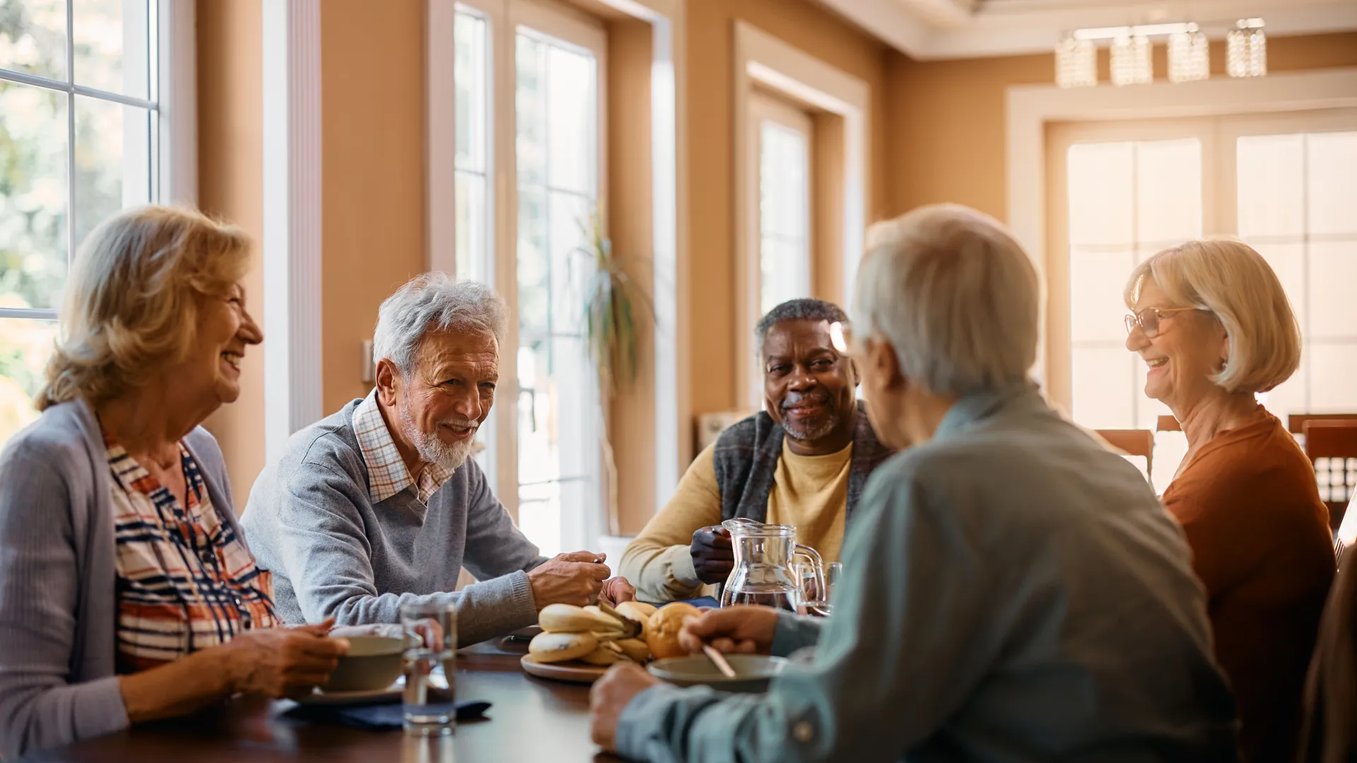 Group of senior friends enjoying coffee and conversation around a dining table in a bright cozy room