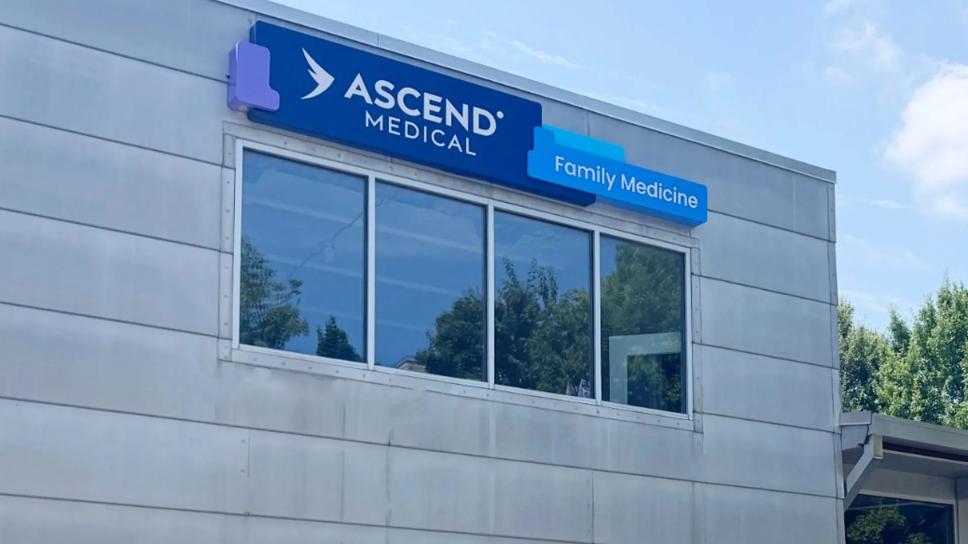Modern Ascend Medical Family Medicine clinic building with large windows and planters under a blue sky.