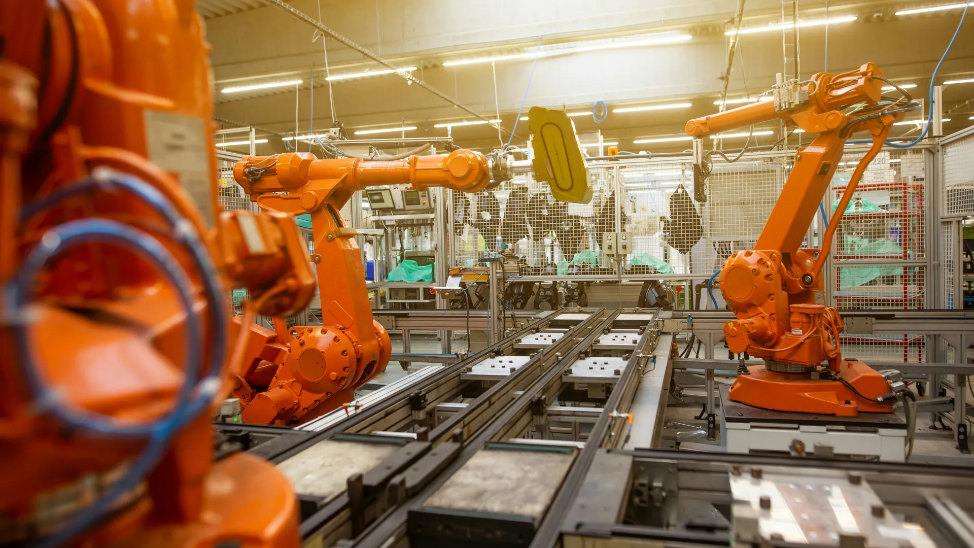 Orange robotic arms operating on automotive assembly line in a modern factory environment with bright lighting