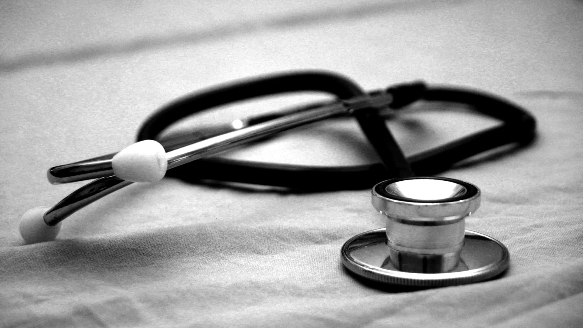 Black and white close-up of a stethoscope lying on a fabric surface, symbolizing healthcare and medicine.