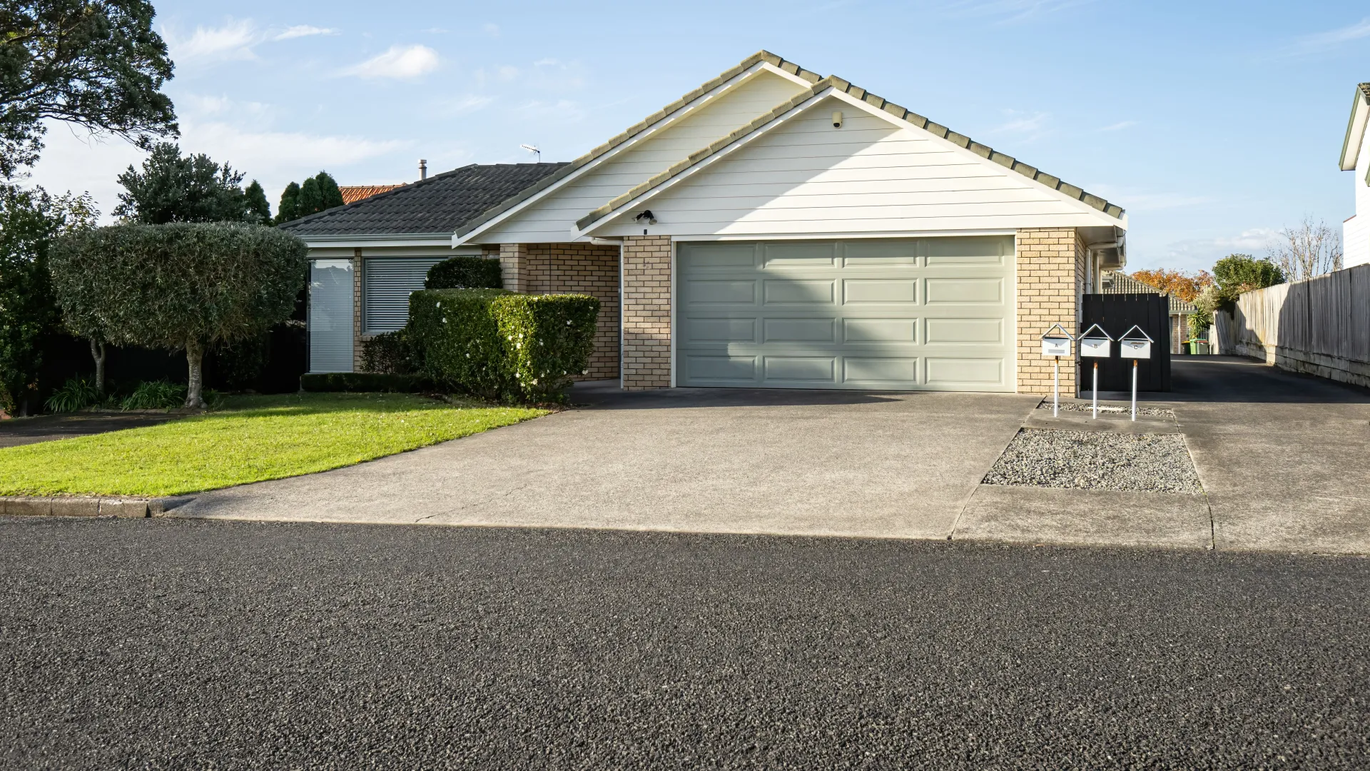 A charming suburban home with a green garage, manicured lawn, and modern mailbox on a sunny day.