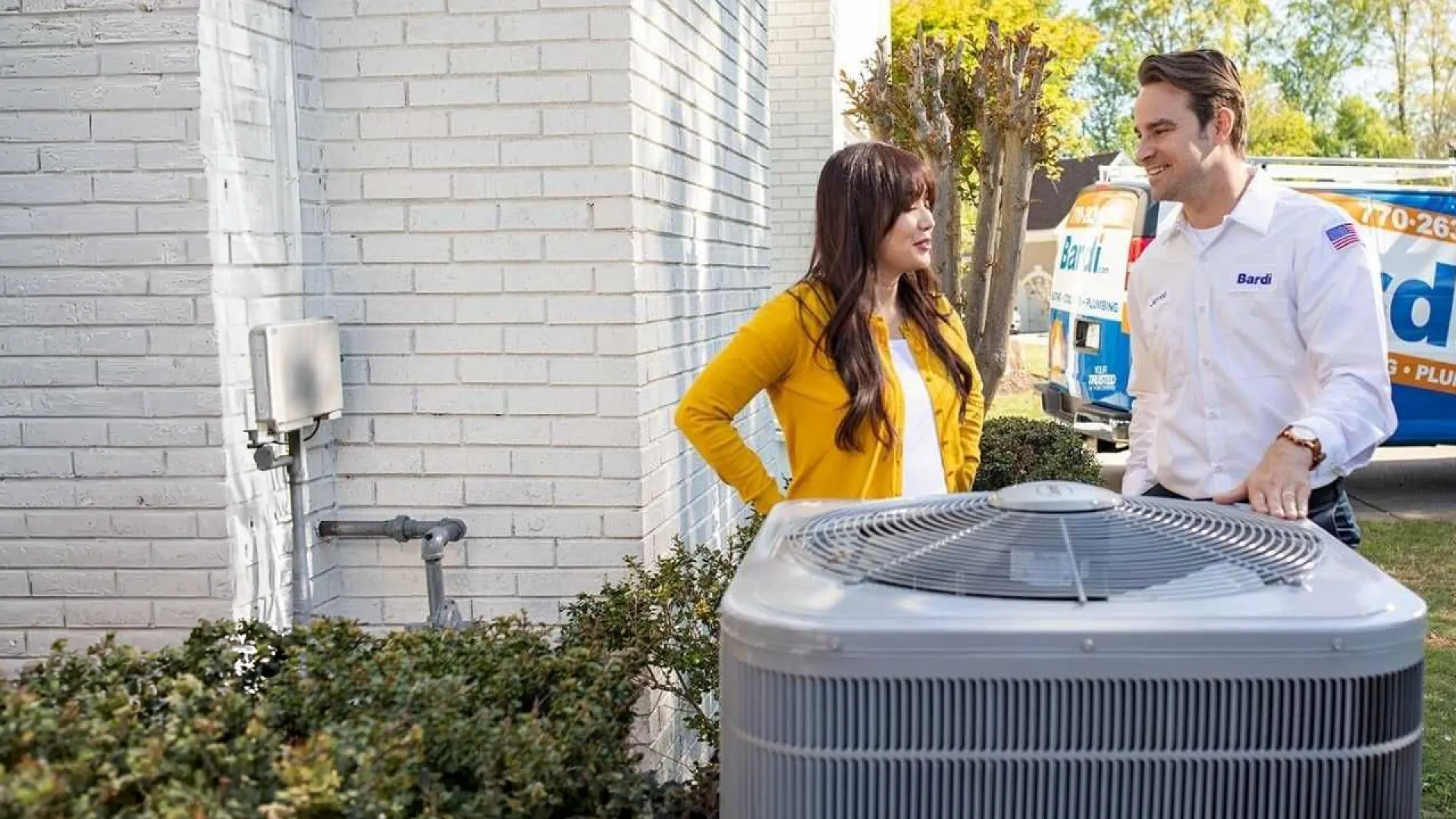 HVAC technician speaking with woman outside next to air conditioning unit and branded service van.
