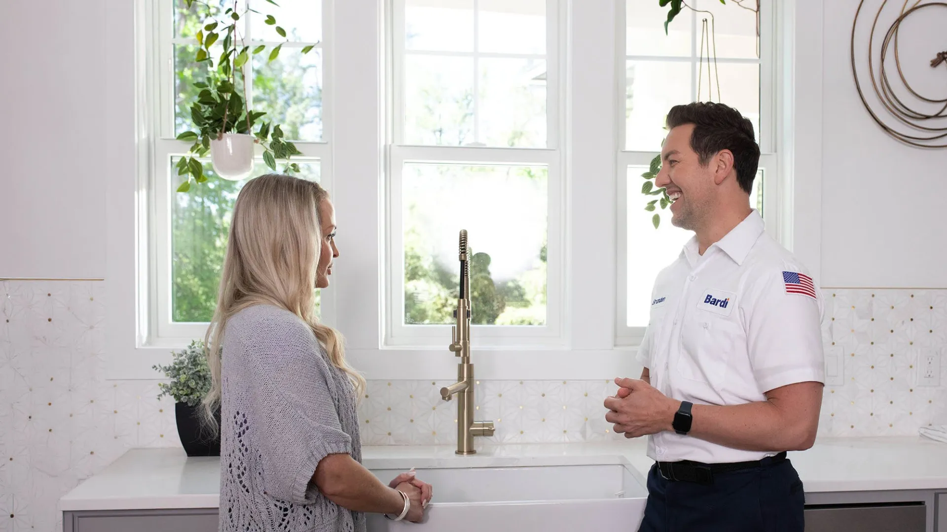Residential drain and sewer plumber in Dunwoody, GA talking to a customer next to a kitchen sink.