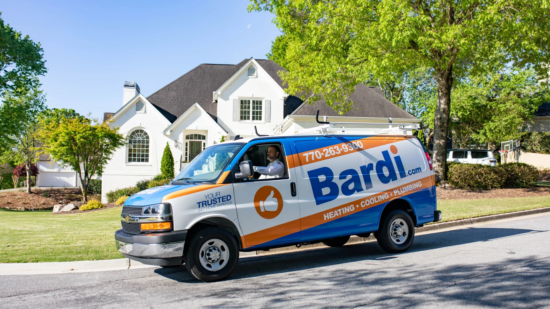 Bardi service van parked on suburban street in front of white house under blue sky with green trees.