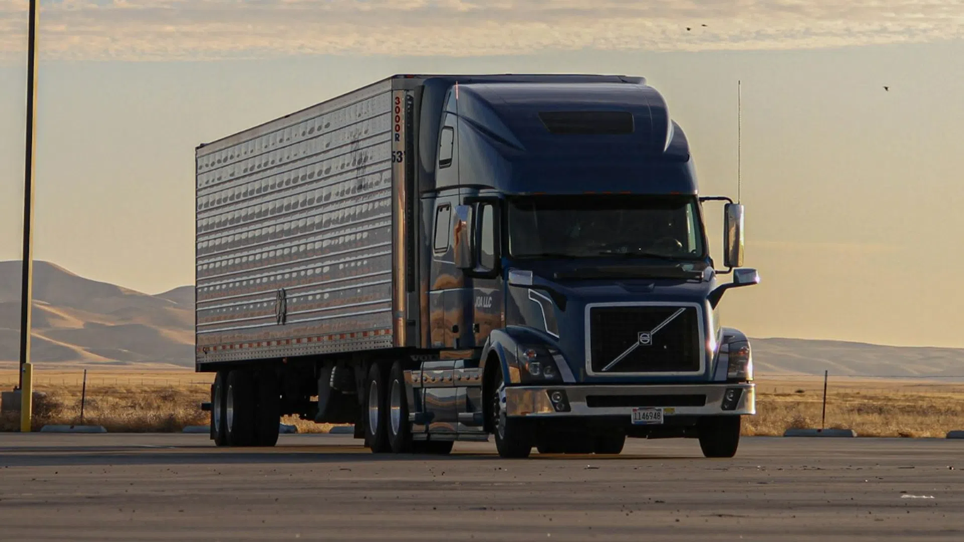 Semi-truck parked on an empty lot with desert hills and a cloudy sky at sunset in the background