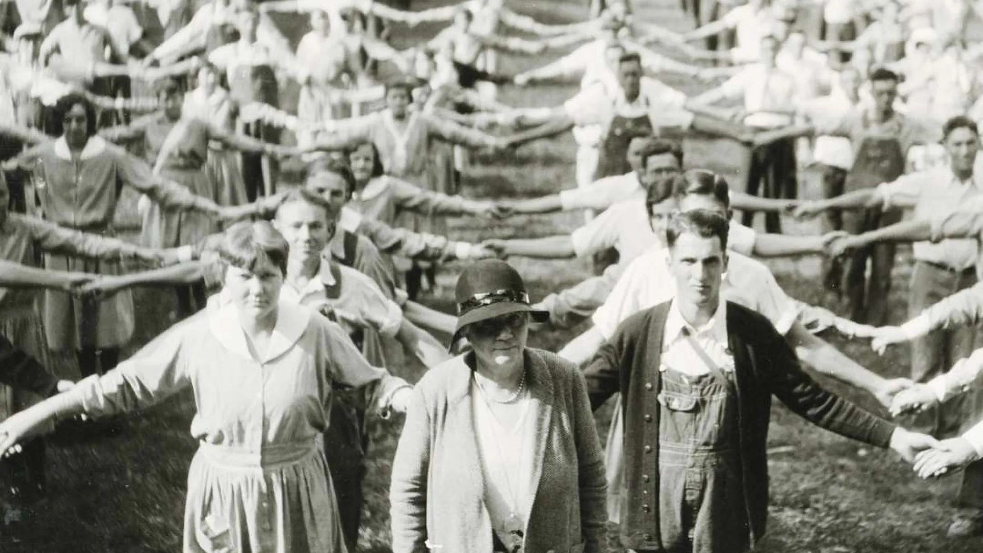Large group of men and women standing in rows outdoors holding hands with arms extended