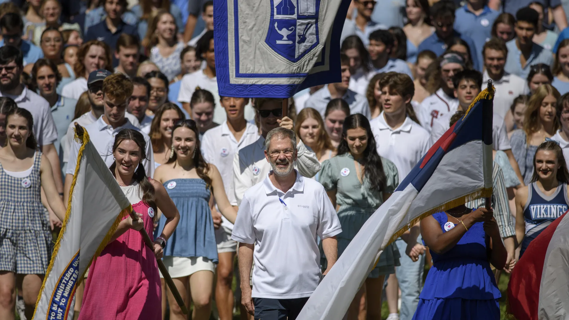 Group of diverse young people and adults in casual summer attire holding flags and walking outdoors on sunny day